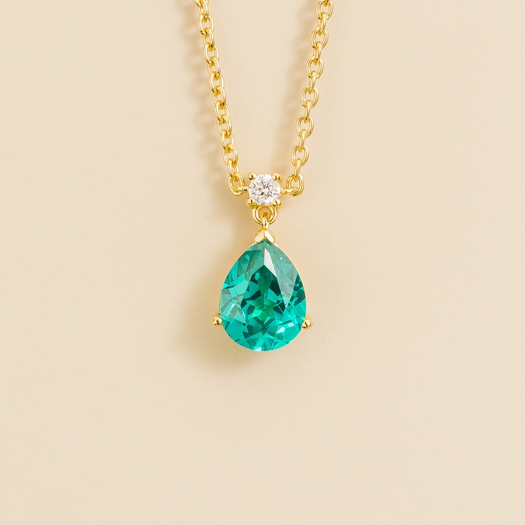 A classic pendant necklace with a pear shape paraiba and round diamond set in gold, displayed against a neutral background.