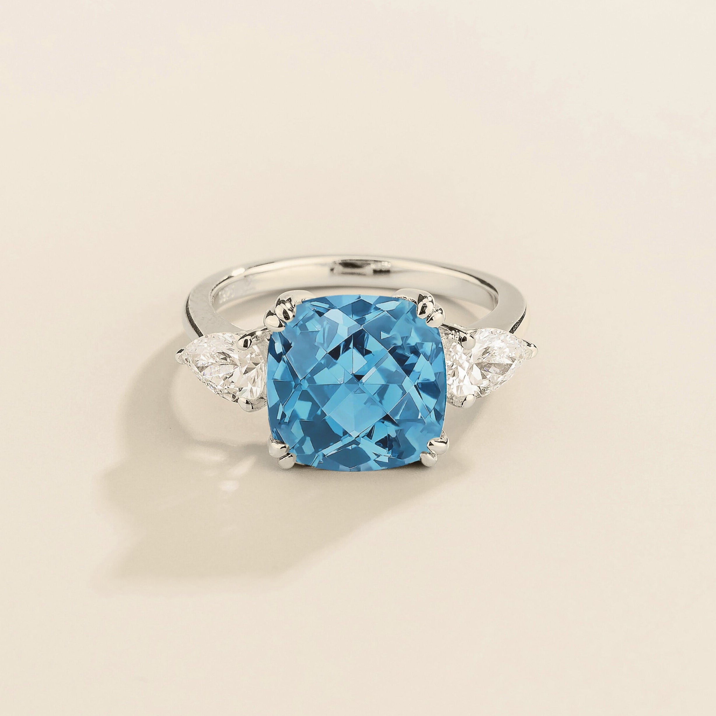 A white gold ring with a large aquamarine cushion-cut centerpiece and smaller pear-cut diamond accents on the sides.