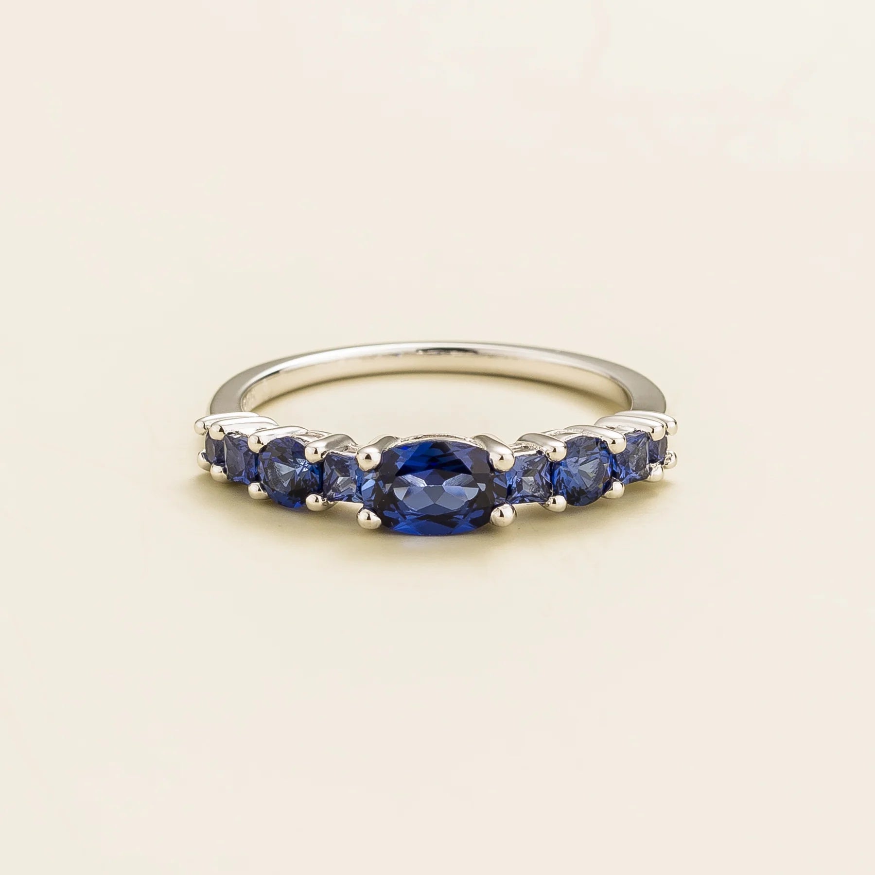 Juvetti white gold ring featuring lab-grown royal blue sapphire in oval, princess, and round cuts for a timeless half-eternity look.