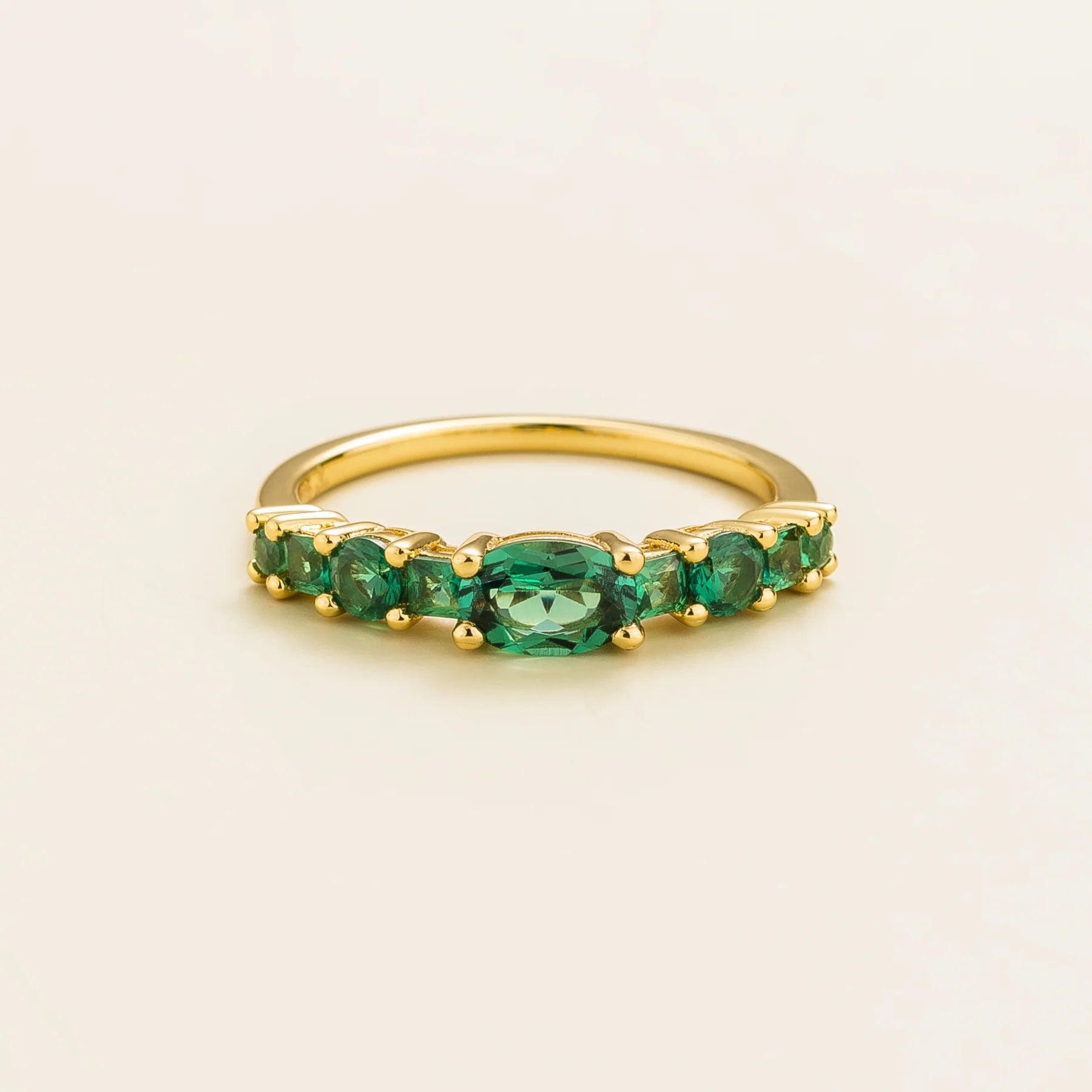 Juvetti yellow gold ring featuring lab-grown emeralds in oval, princess, and round cuts for a timeless half-eternity look.