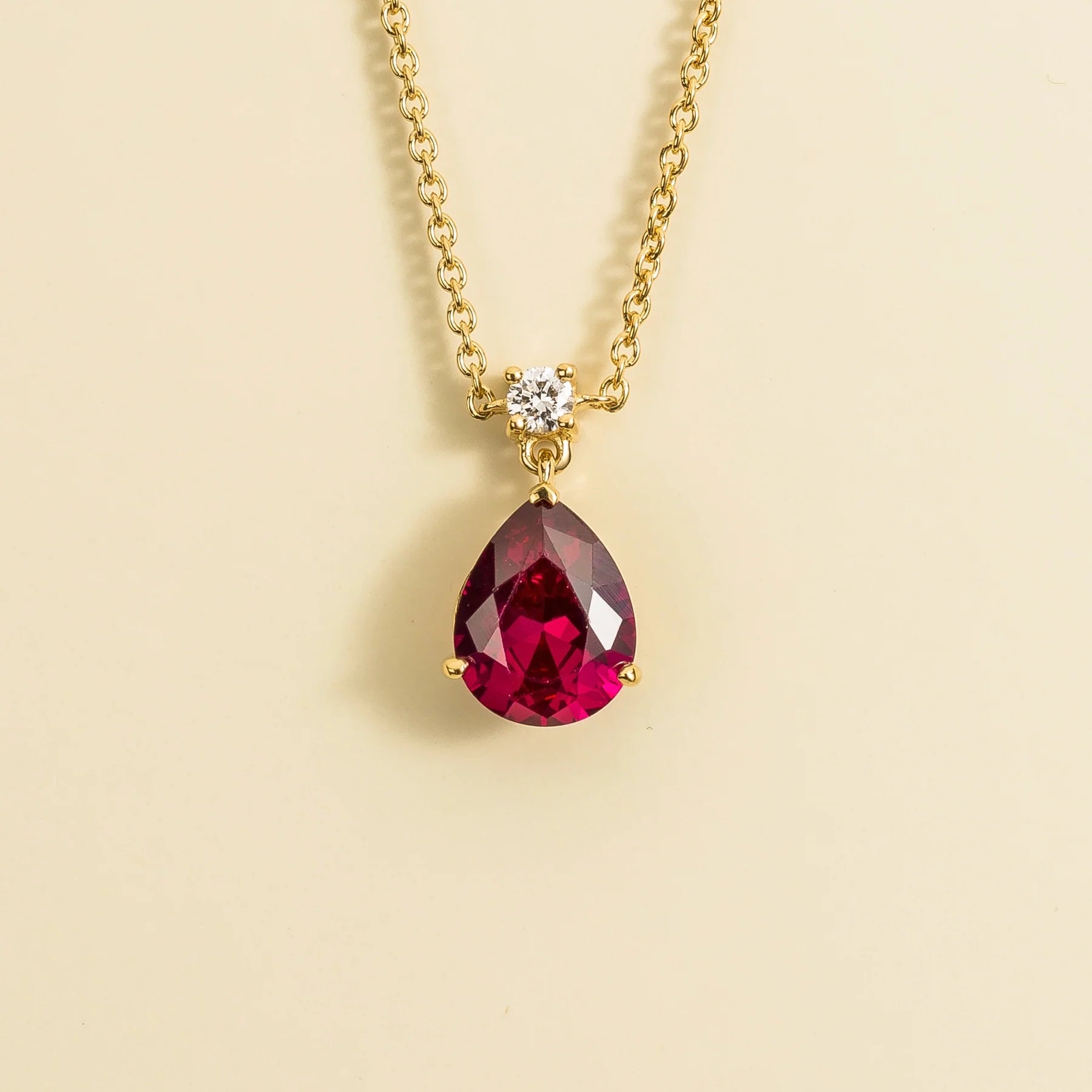 A classic pendant necklace with a pear shape ruby and round diamond set in white gold, displayed against a neutral background. Juvetti jewellery London