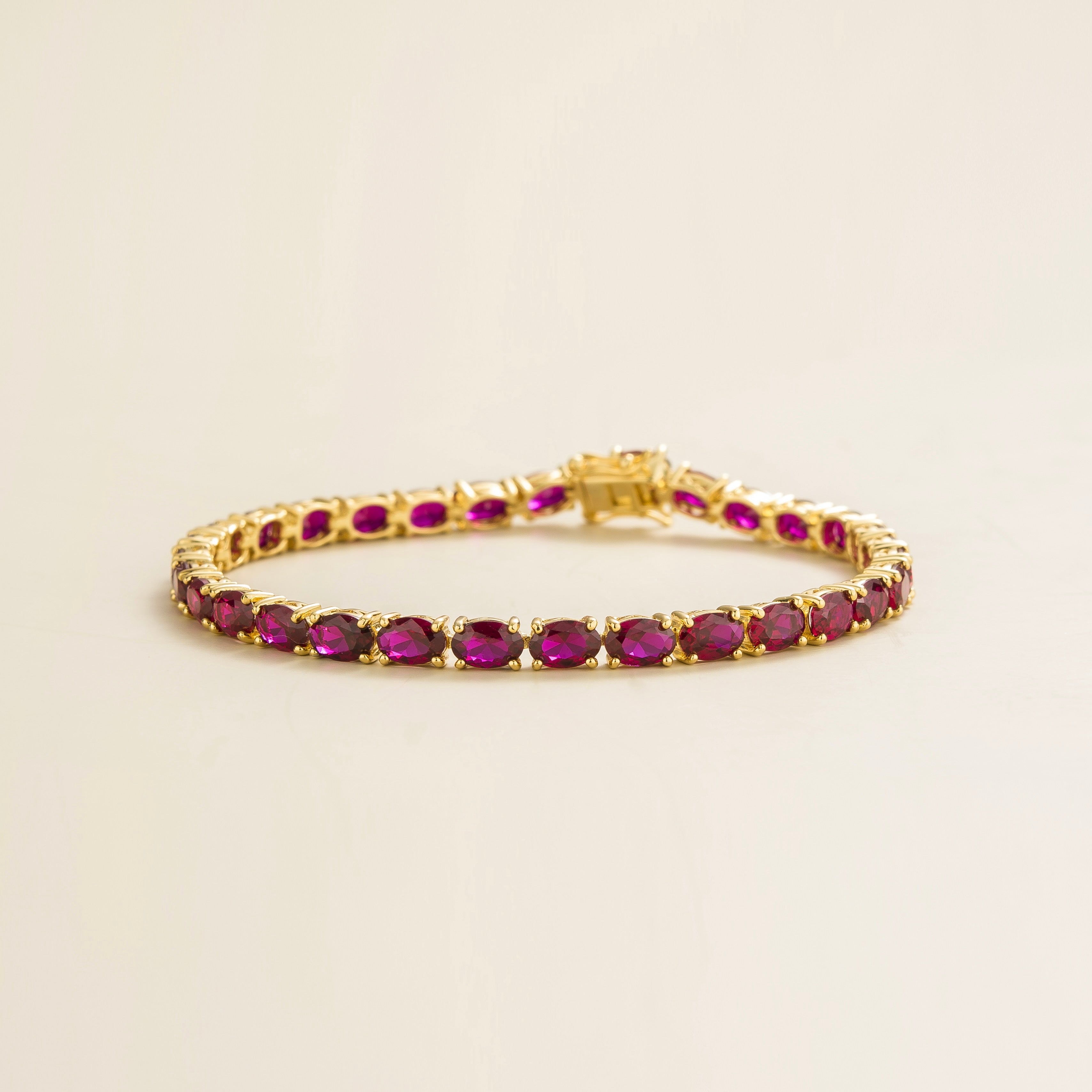 A gold tennis bracelet set with oval-shaped ruby gemstones. Best London Jewellery Store