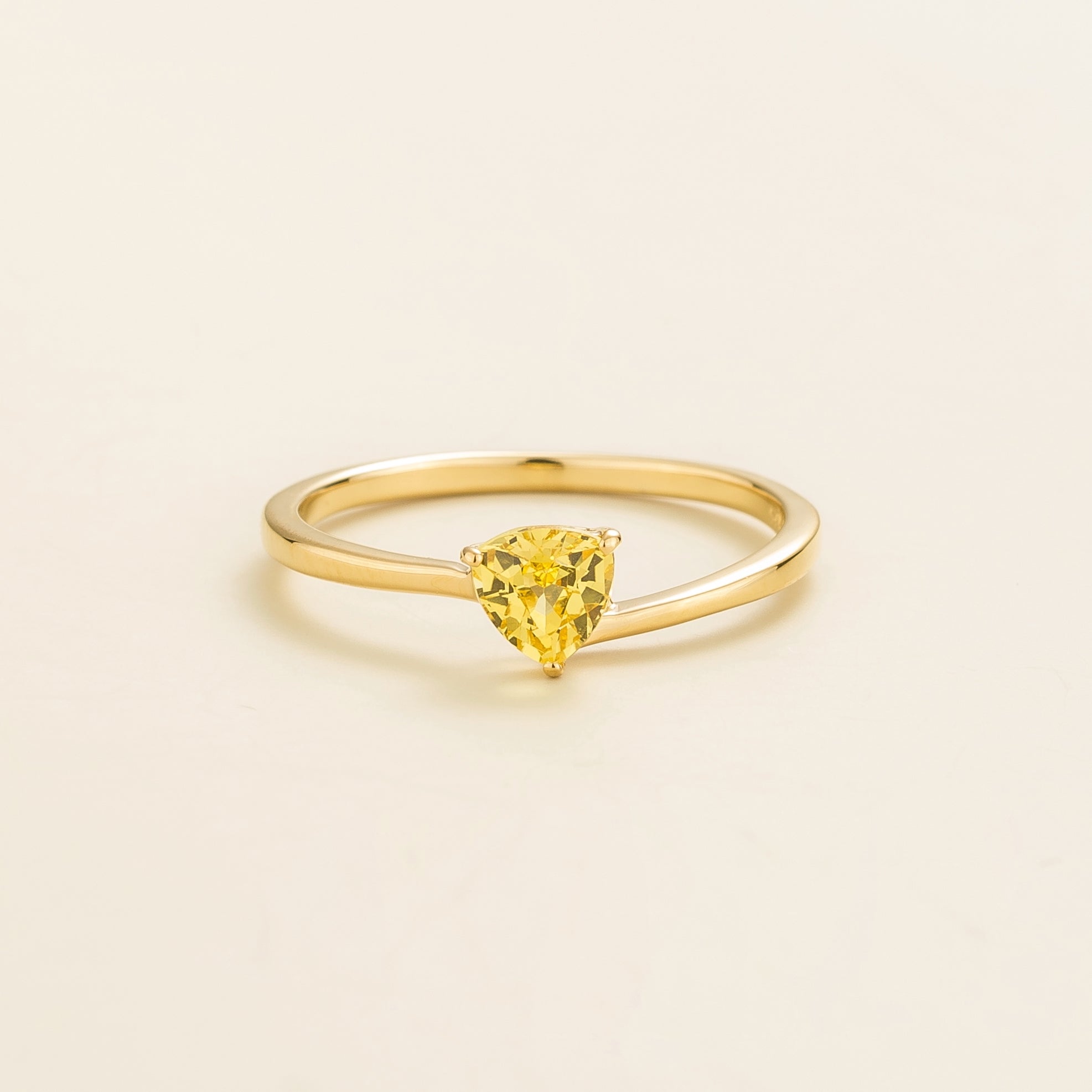 A solitaire gold ring with a trillion-cut yellow sapphire in a curved modern setting on a plain background.