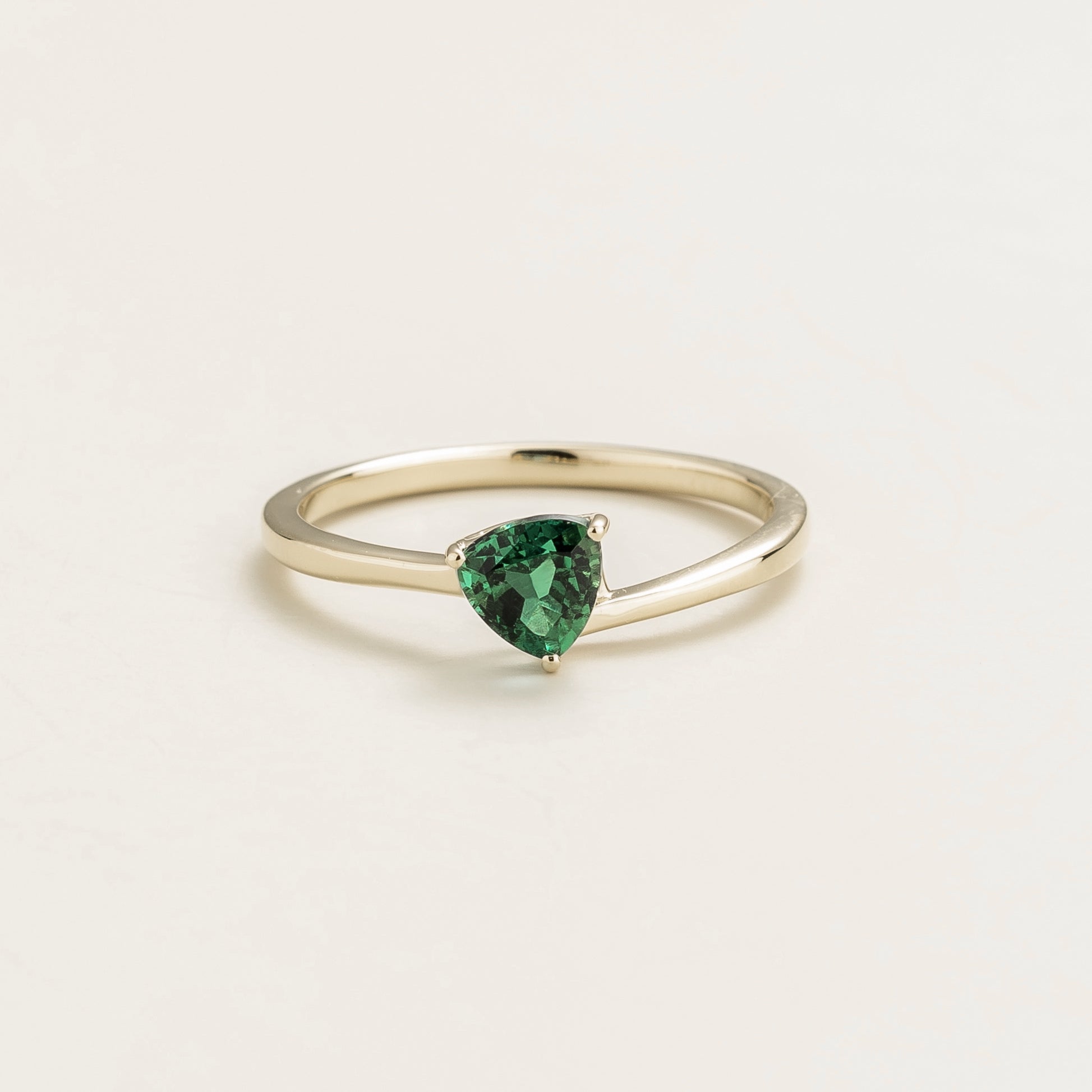 A solitaire white gold ring with a trillion-cut emerald in a curved setting on a plain background.