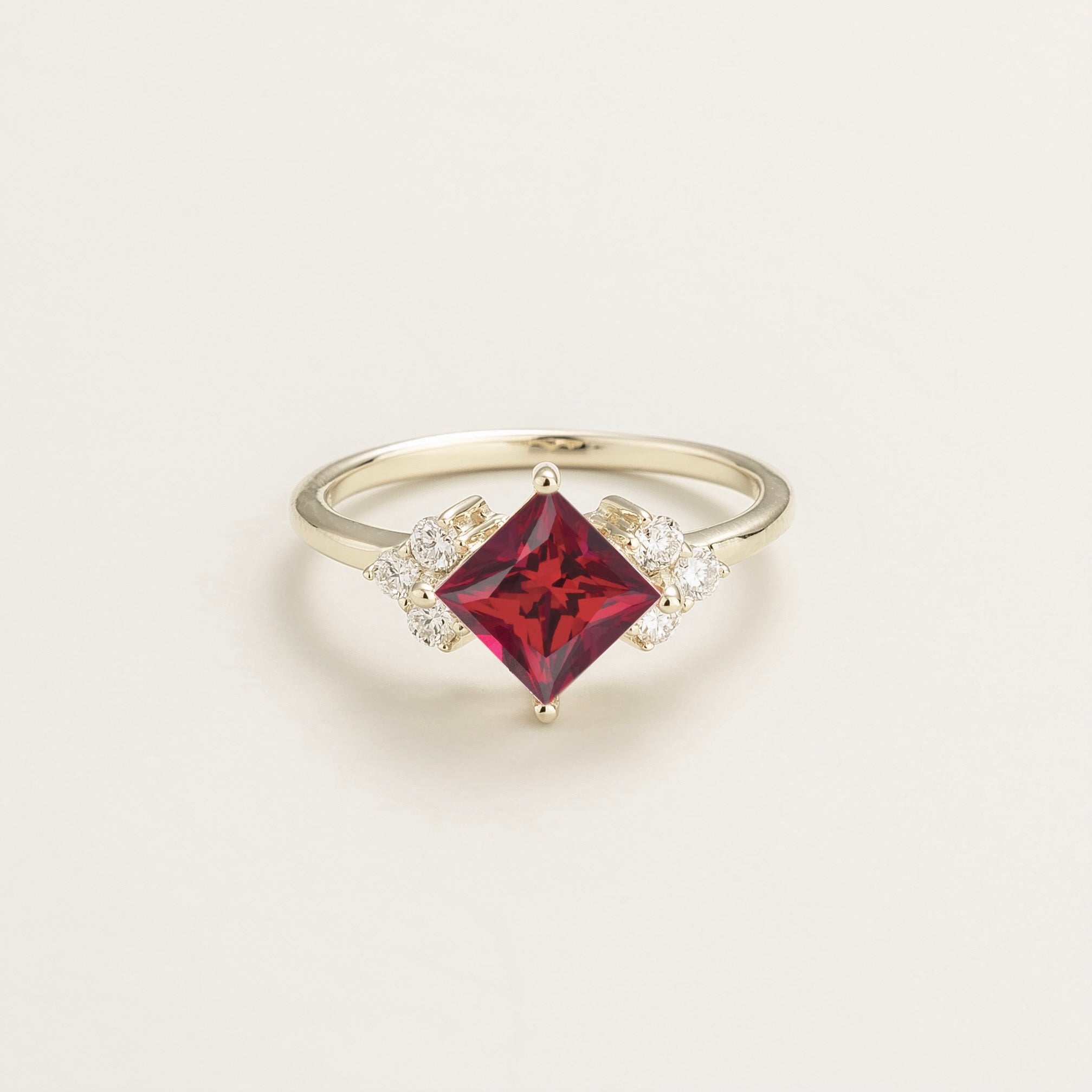 A white gold ring featuring a princess cut ruby center stone flanked by smaller diamond stones on either side.