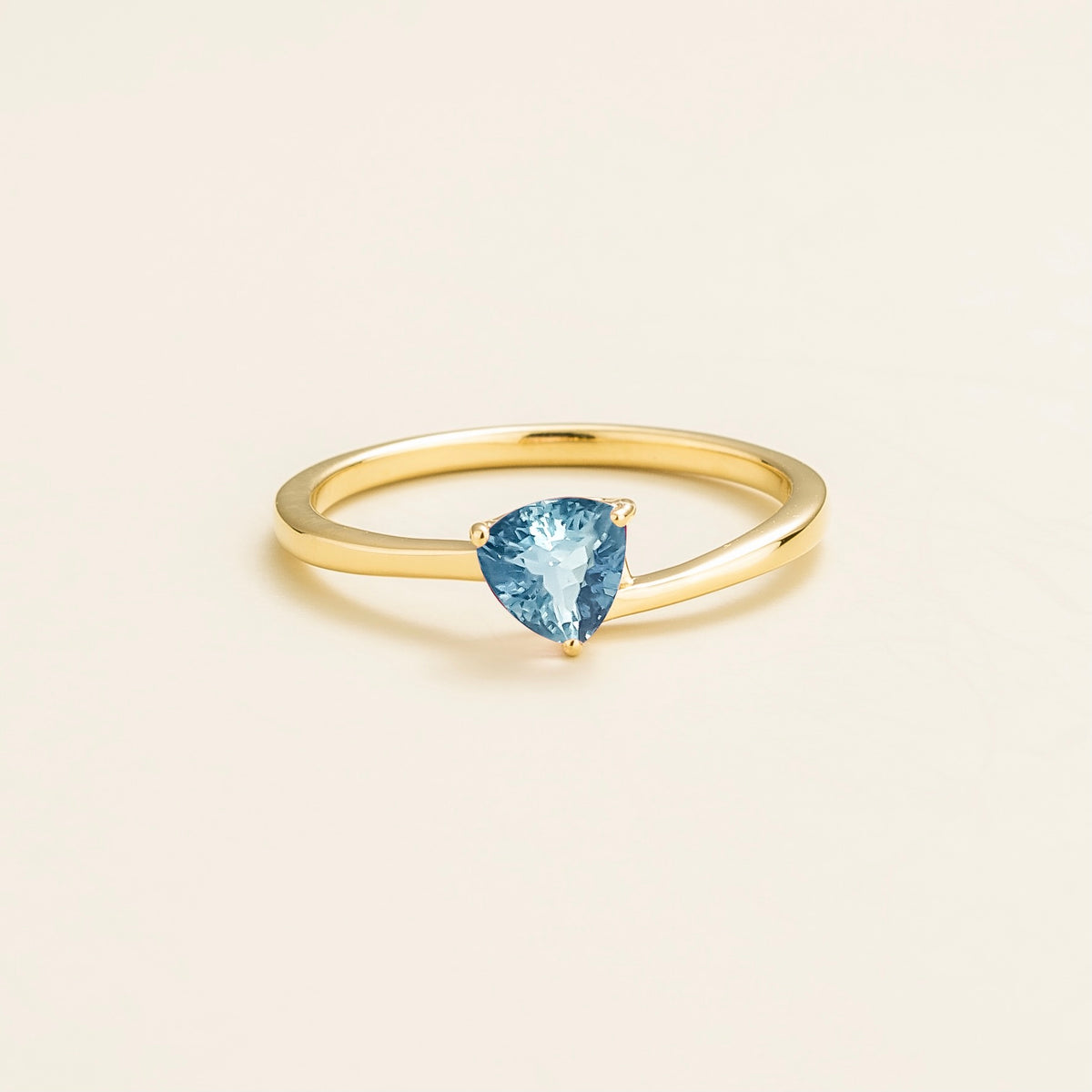A solitaire gold ring with a trillion-cut aquamarine in a curved setting, displayed against a light background.