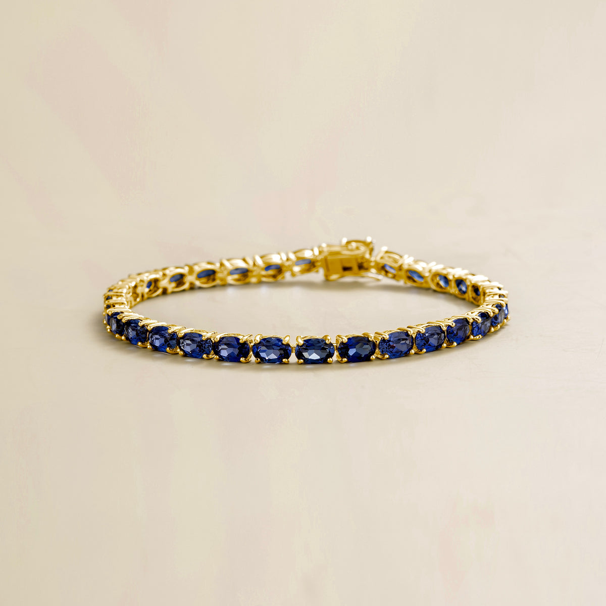 A gold tennis bracelet set with oval blue sapphire gemstones.