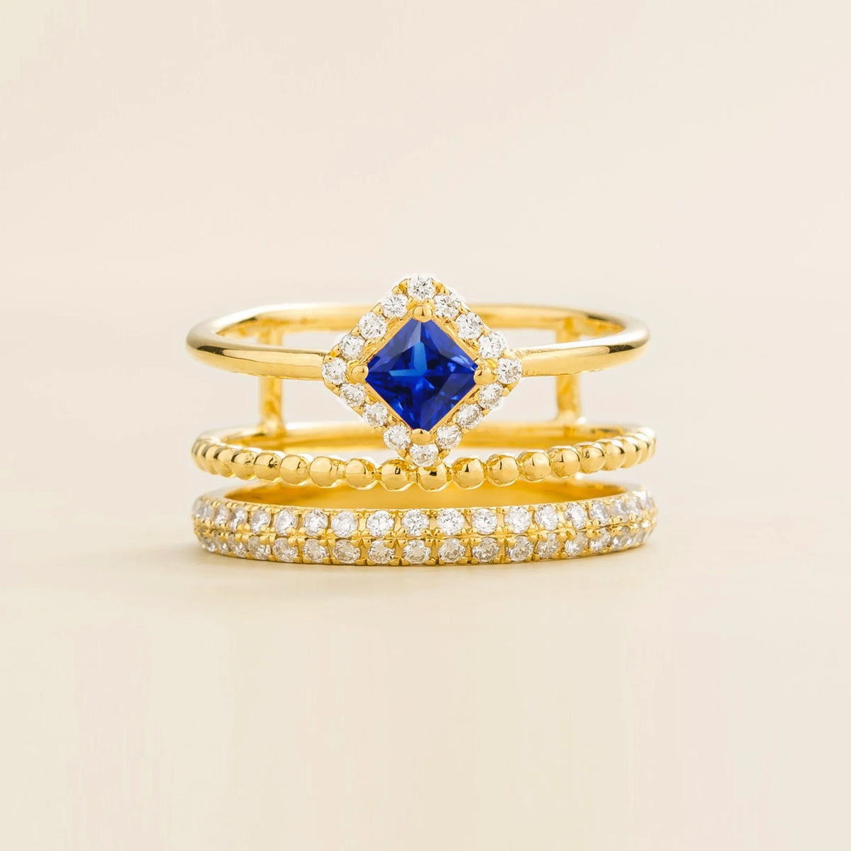 Amici triple-band stacking ring in gold, princess-cut lab-grown blue sapphire in a diamond halo with beaded and pavé bands, front view | Juvetti London
