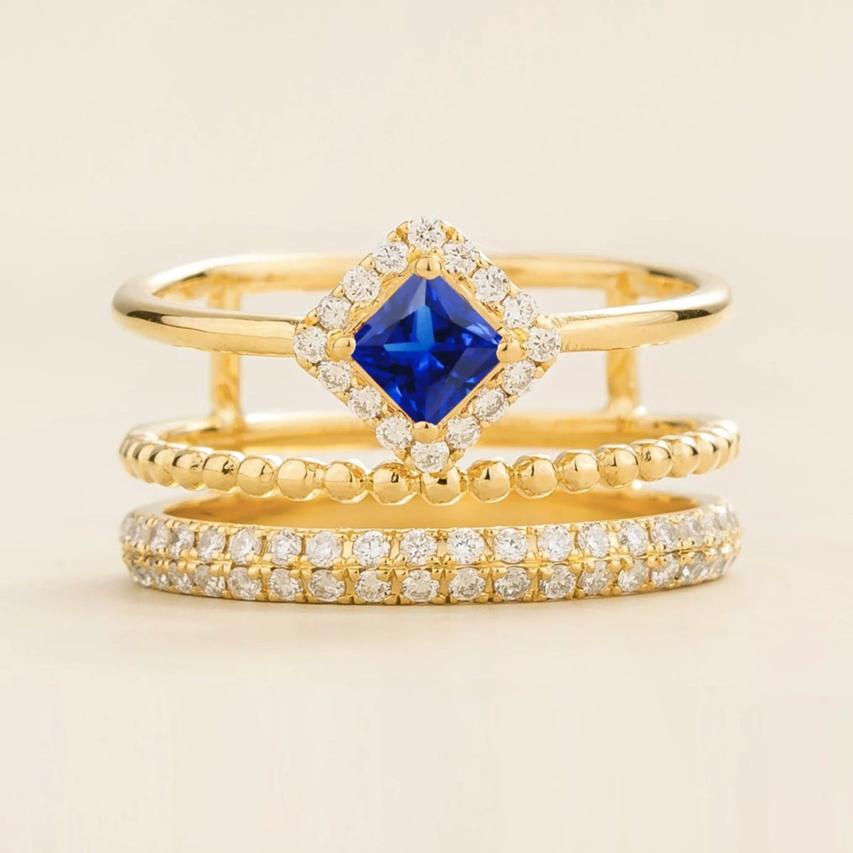 Amici triple-band stacking ring in gold, princess-cut lab-grown blue sapphire in a diamond halo with beaded and pavé bands, front view | Juvetti London