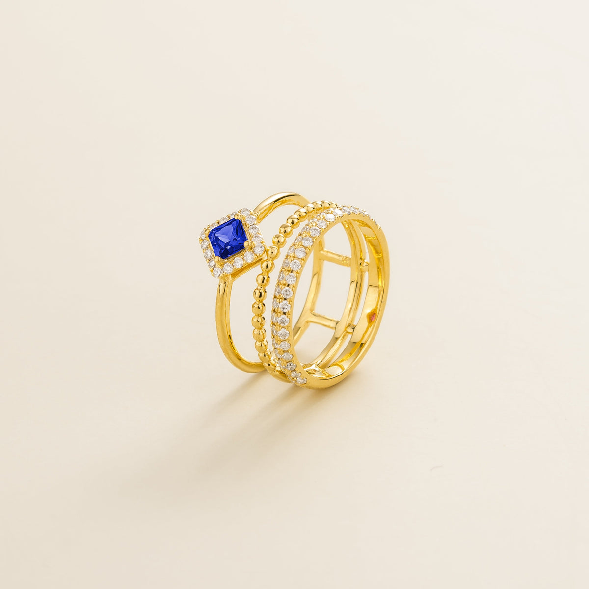 Amici triple-band stacking ring in gold, princess-cut lab-grown blue sapphire in a diamond halo with beaded and pavé bands, side view | Juvetti London