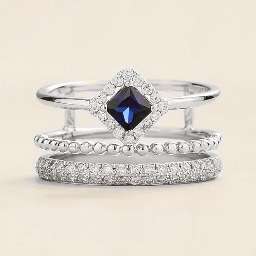 Amici triple-band stacking ring in white gold, princess-cut lab-grown blue sapphire in a diamond halo with beaded and pavé bands, front view | Juvetti London