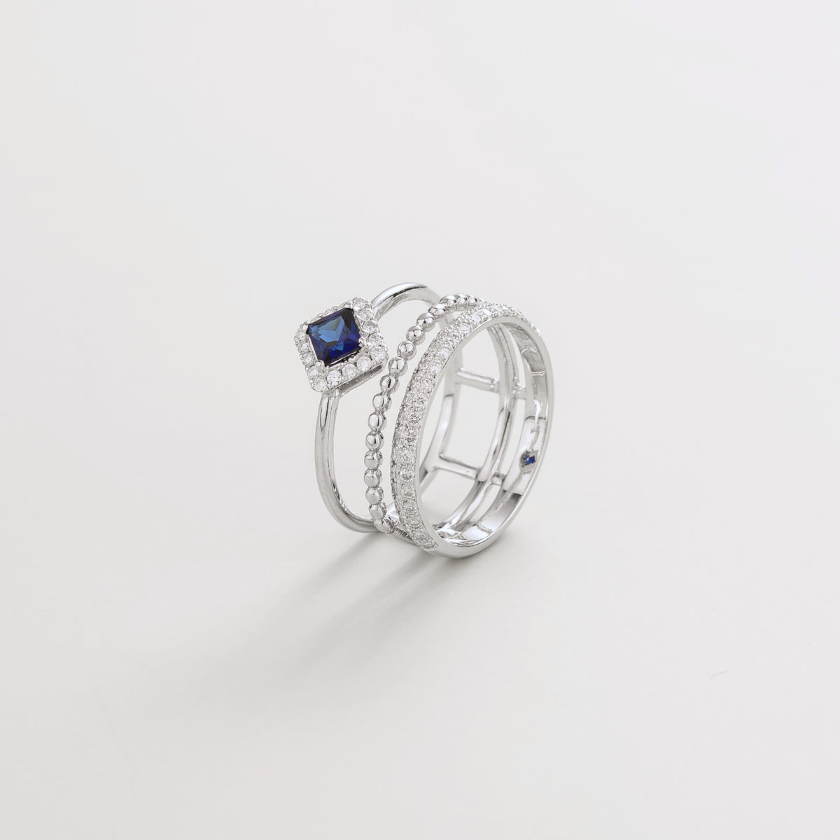 Amici triple-band stacking ring in white gold, princess-cut lab-grown blue sapphire in a diamond halo with beaded and pavé bands, side view | Juvetti London