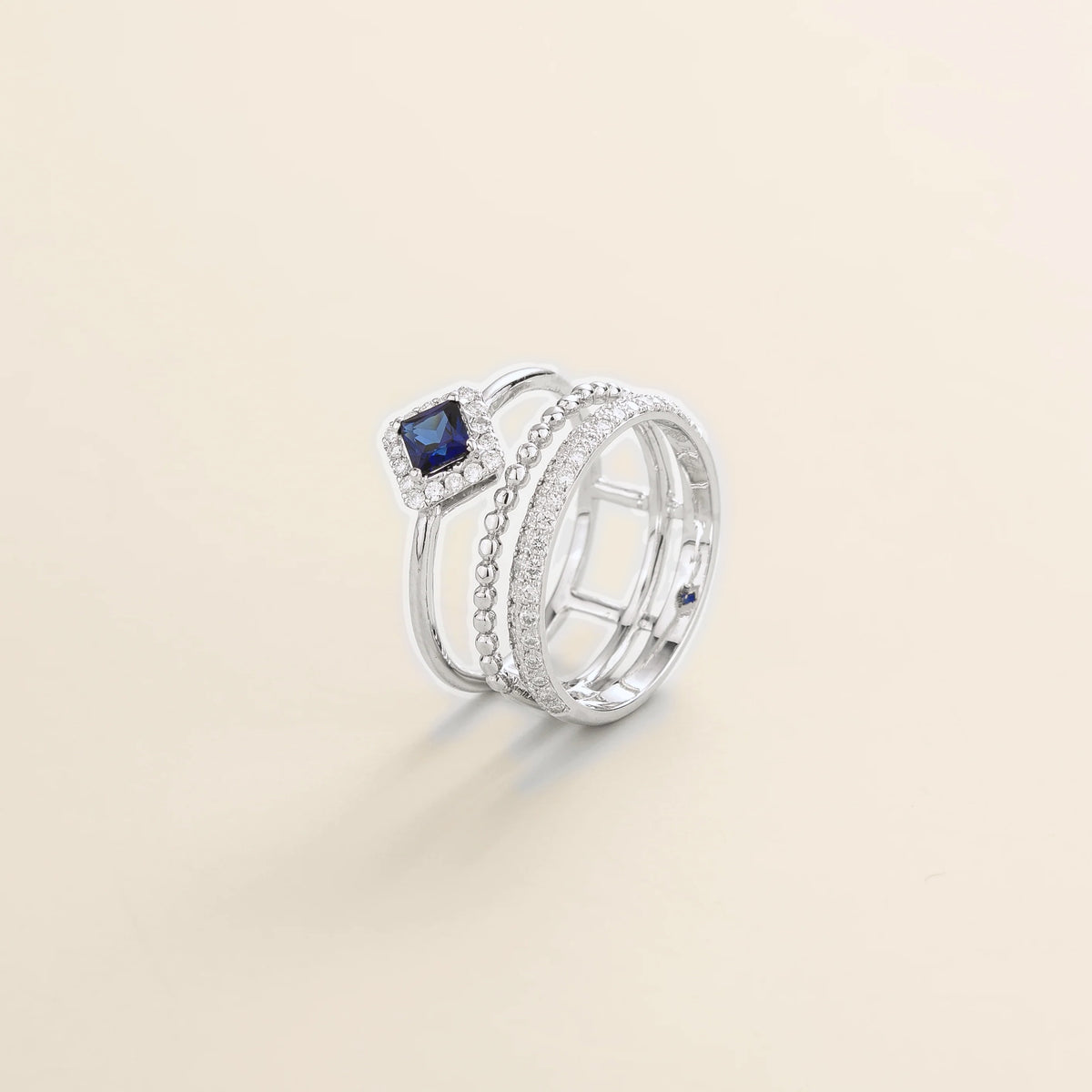 Amici triple-band stacking ring in white gold, princess-cut lab-grown blue sapphire in a diamond halo with beaded and pavé bands, side view | Juvetti London