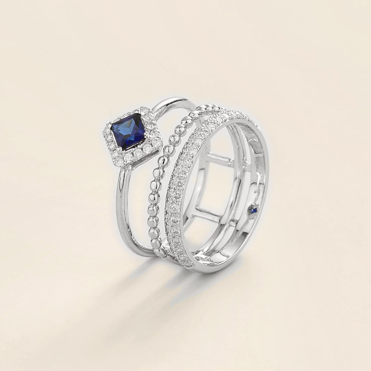 Amici triple-band stacking ring in white gold, princess-cut lab-grown blue sapphire in a diamond halo with beaded and pavé bands, side view | Juvetti London
