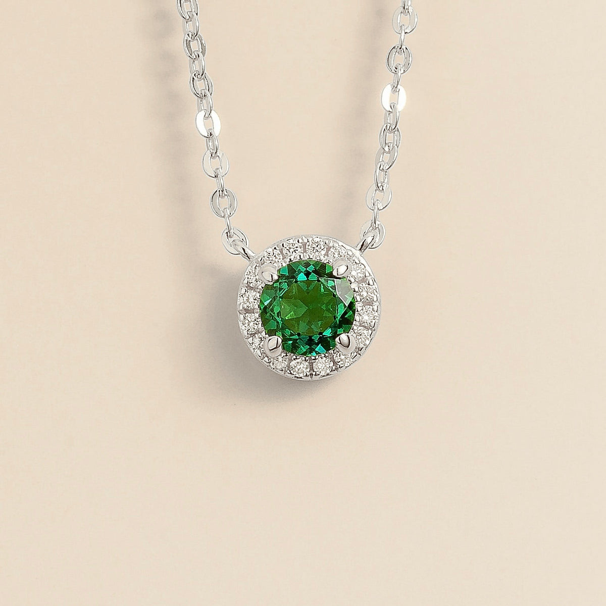 A white gold necklace with a central round emerald surrounded by halo diamonds, displayed against a light background.