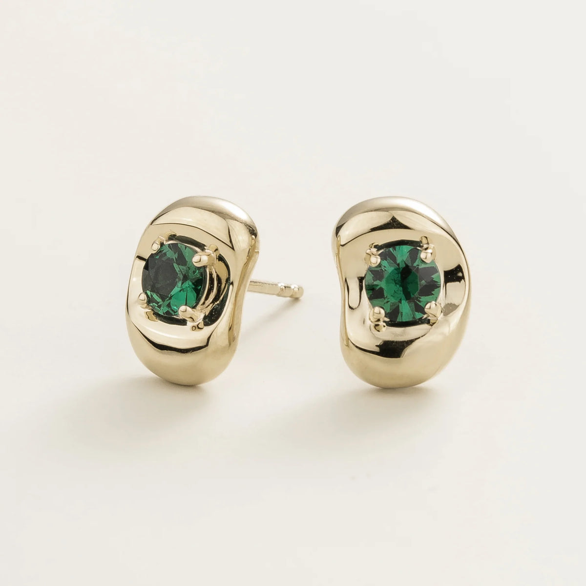 Fava round lab-grown emerald stud earrings in white gold, sculpted pebble setting, angled view | Juvetti London