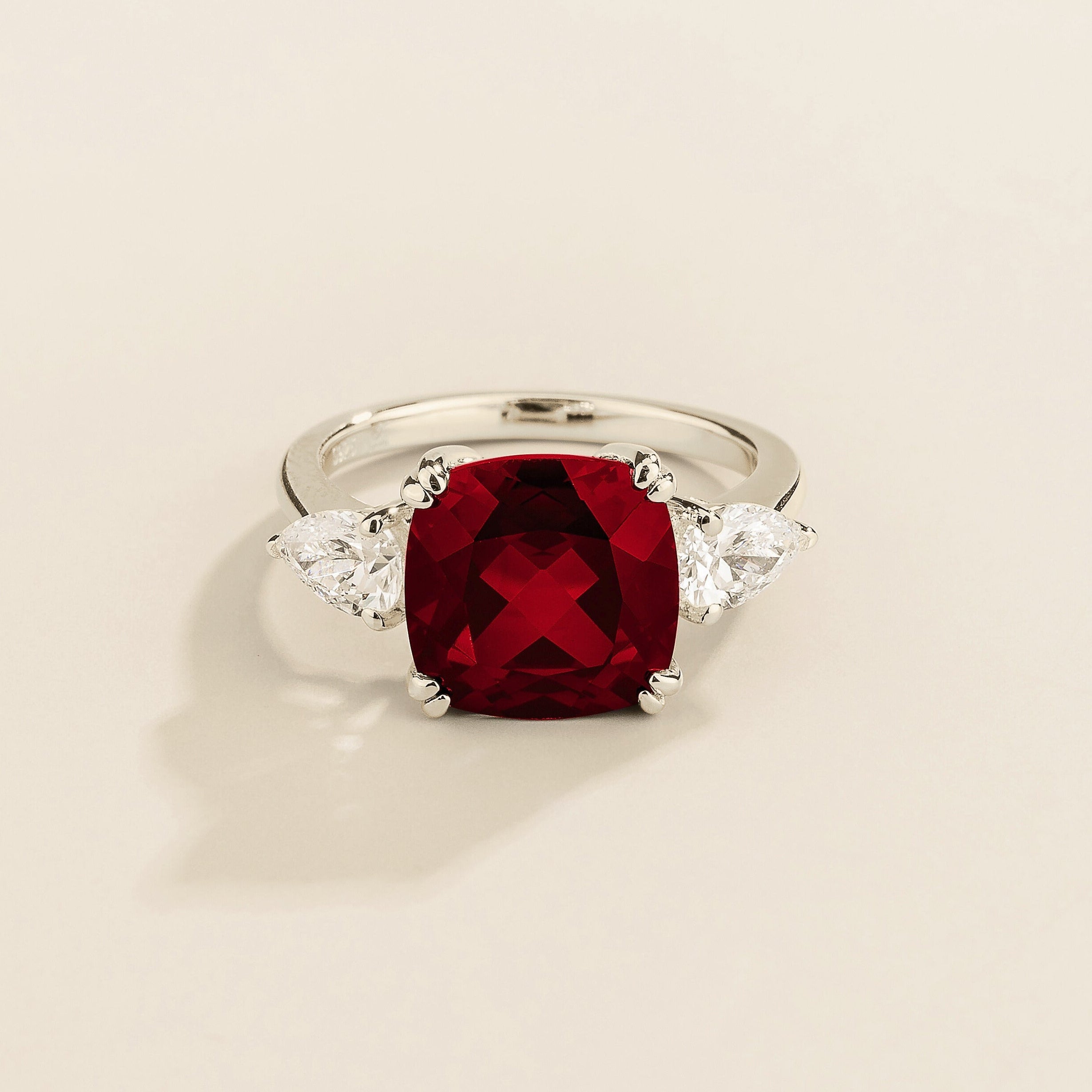 Gold ring with cushion cut ruby gemstone and pear side diamonds on a beige background