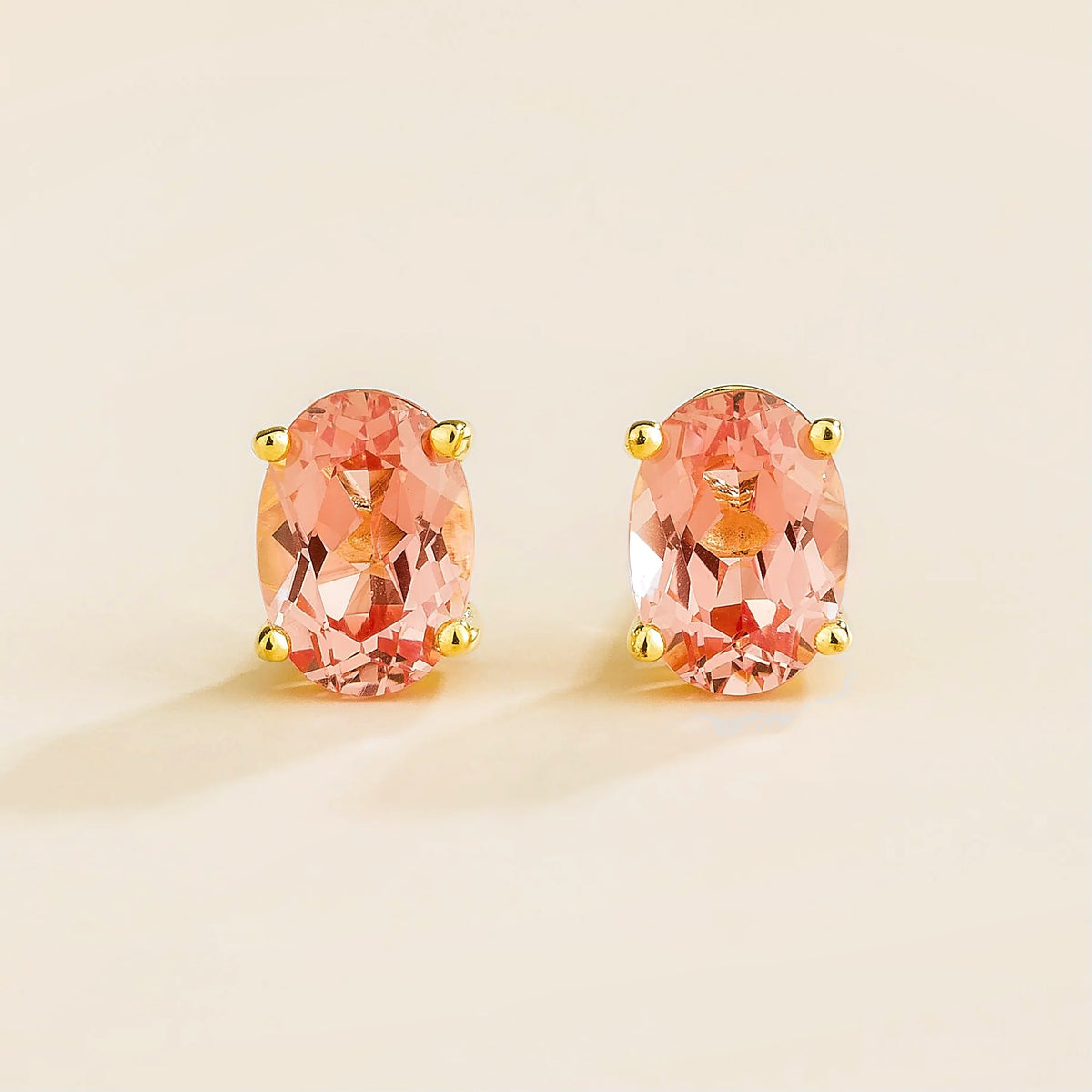 A pair of stud gold earrings set with oval Padparadscha sapphires.
