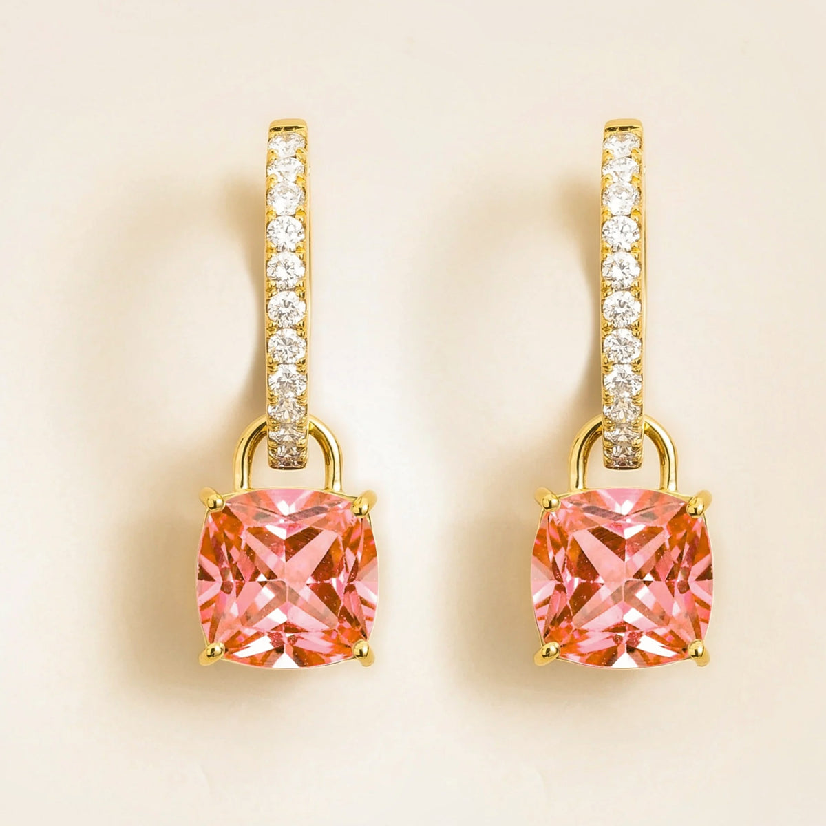 A pair of yellow gold drop earrings featuring cushion-cut Padparadscha sapphires with smaller diamonds along the hoop.