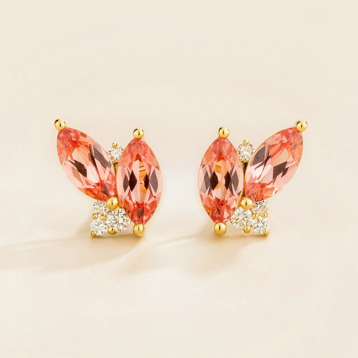 Pair of earrings with marquis padparadscha sapphire gemstones and gold with diamond accents on a light background
