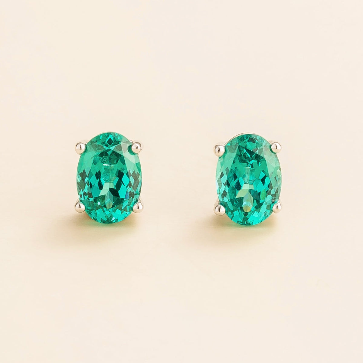 A pair of white gold hoop earrings set with oval-shaped Paraiba gemstones.