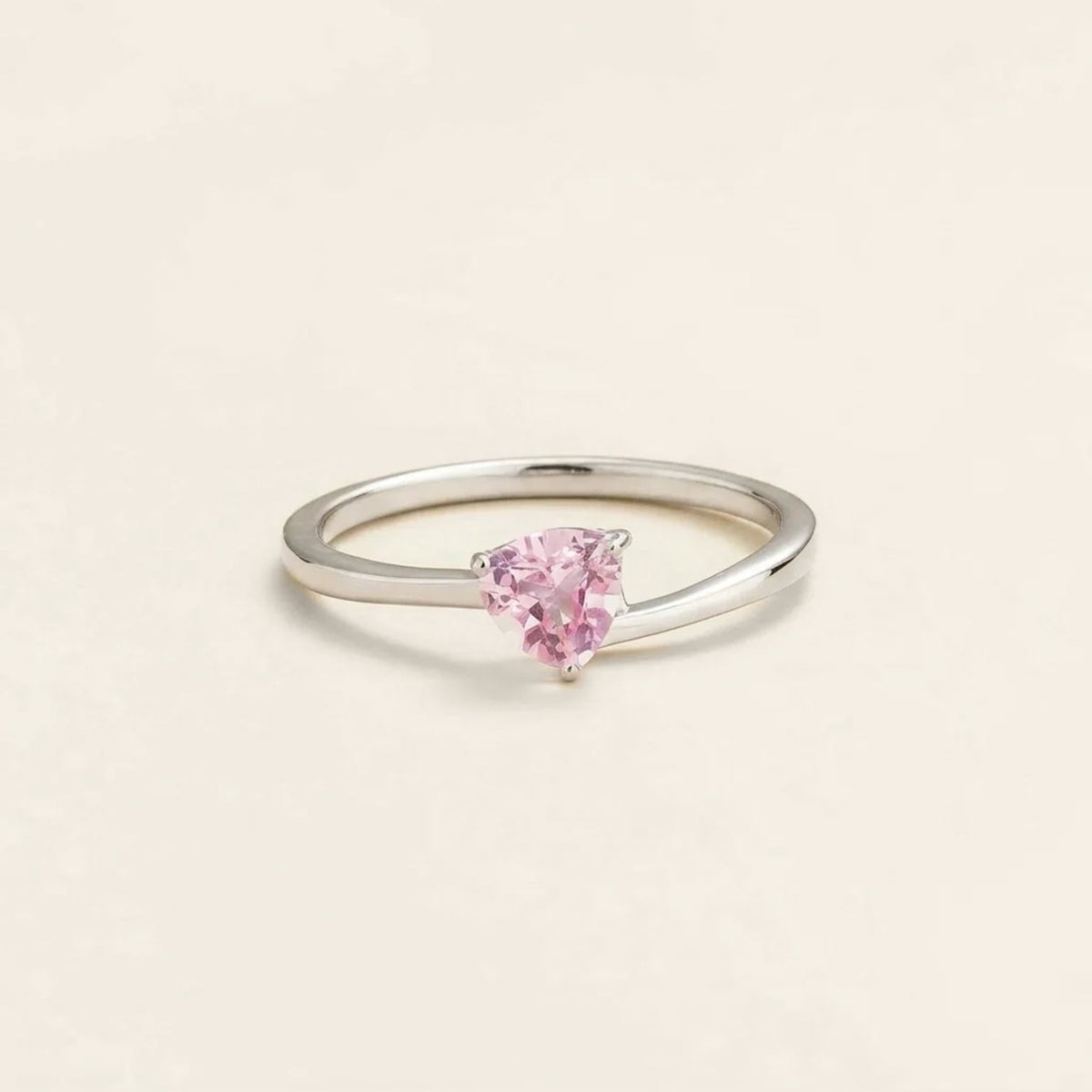 A white gold solitaire ring with a trillion-cut pink sapphire in a curved setting on a plain background.