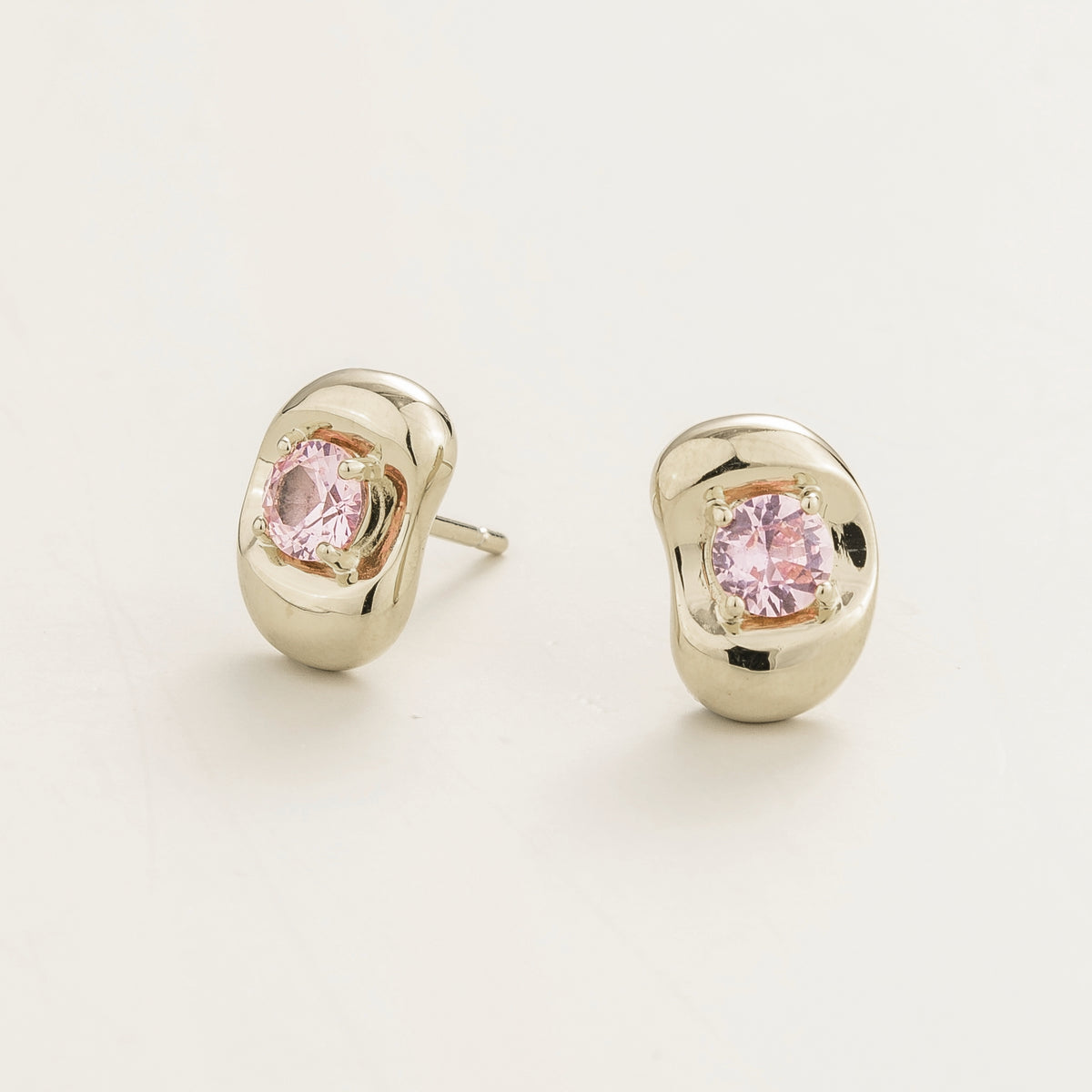 Fava round lab-grown pink sapphire stud earrings in white gold, sculpted pebble setting, angled view | Juvetti London