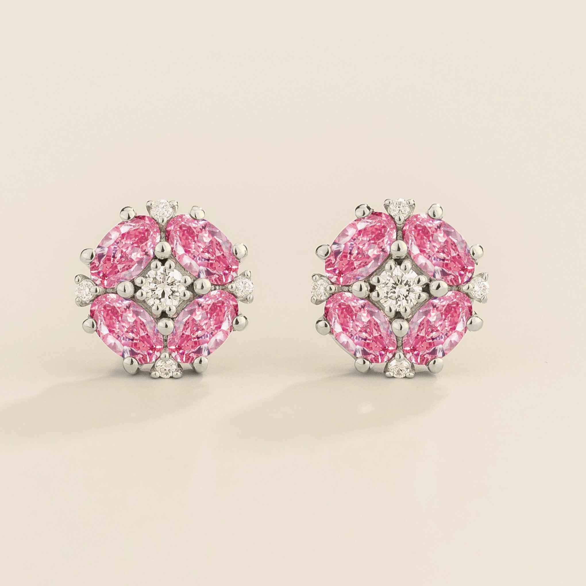 A pair of white gold earrings featuring oval pink sapphires and round diamonds arranged in a floral pattern.