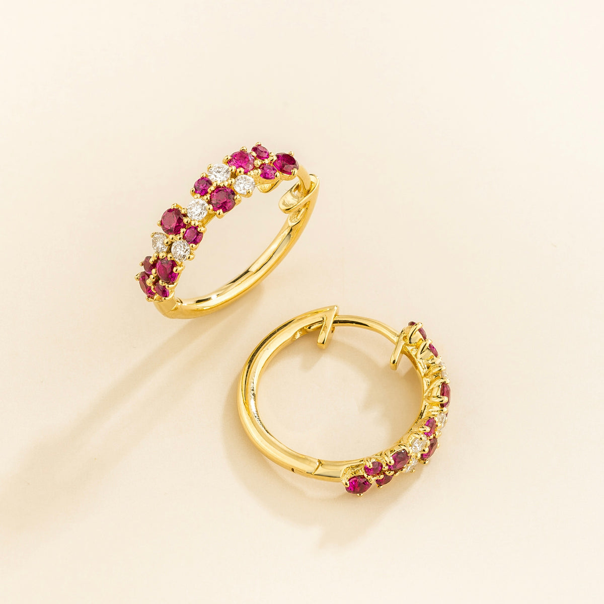 A pair of yellow gold huggie earrings set with cluster of round ruby and diamond accents, displayed against a neutral background.