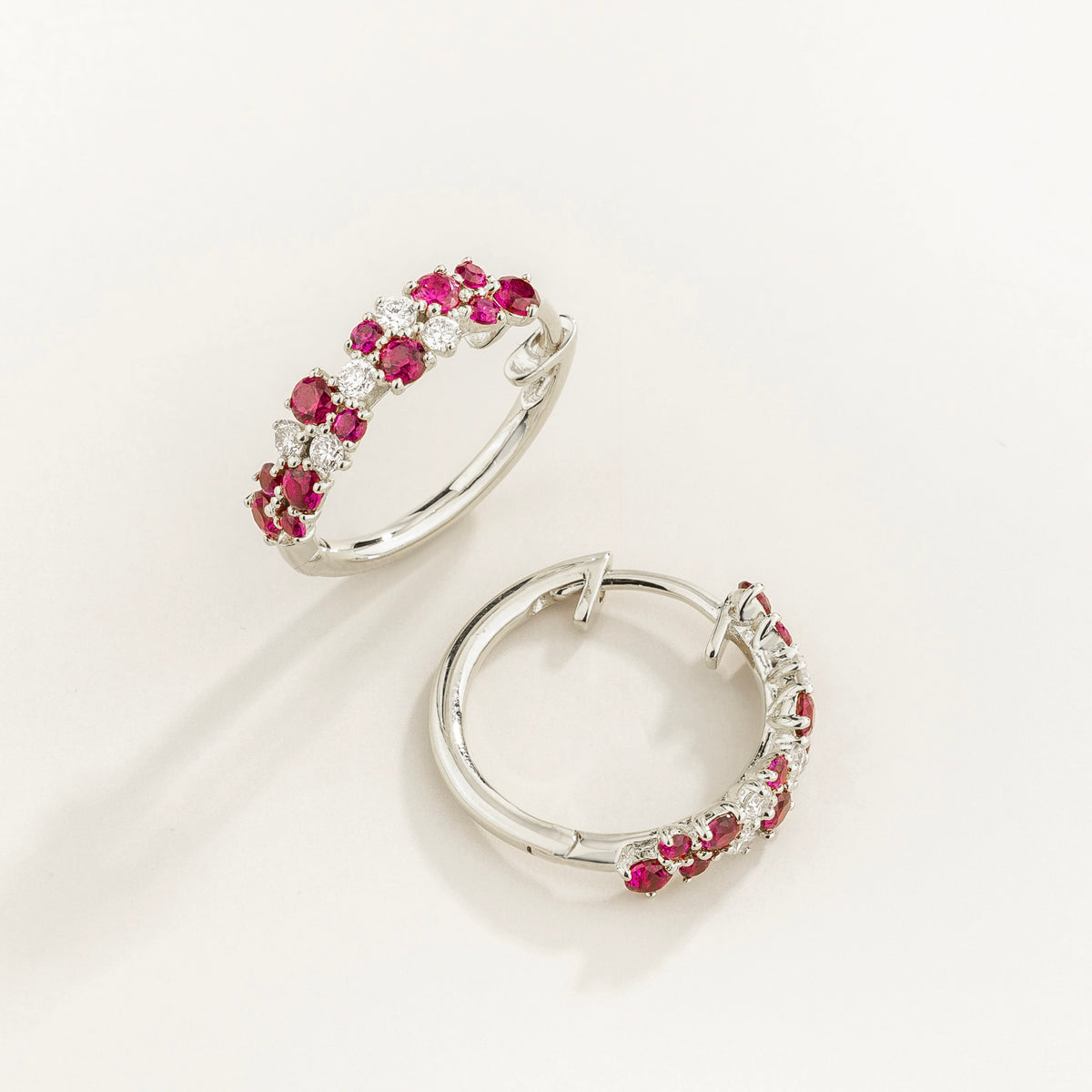 A pair of white gold huggie earrings set with cluster of round ruby and diamond accents, displayed against a neutral background.