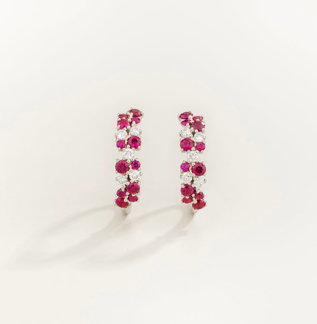 Pair of ruby and diamond huggie hoop earrings on a white background