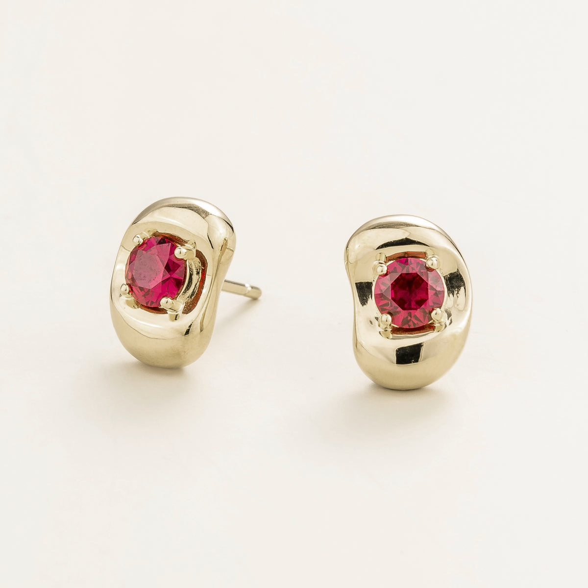 Fava round lab-grown ruby stud earrings in white gold, sculpted pebble setting, angled view | Juvetti London