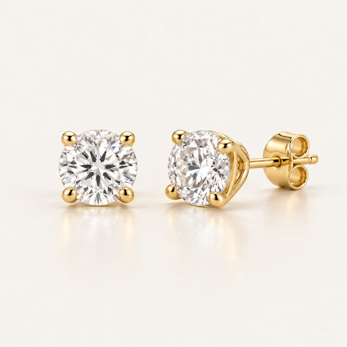 Pair of solitaire stud earring settings in yellow gold with four rounded claws and butterfly backs, shown with 1 ct round diamonds