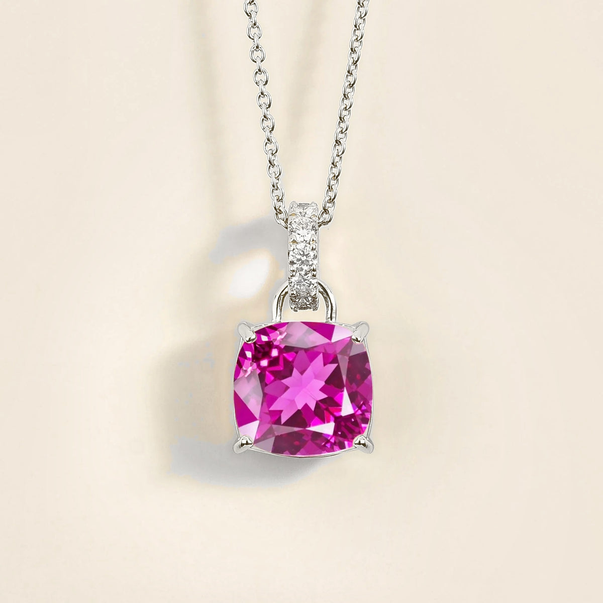 A white gold necklace featuring a vivid pink sapphire pendant with smaller diamonds, set in a cushion-shaped pendant.