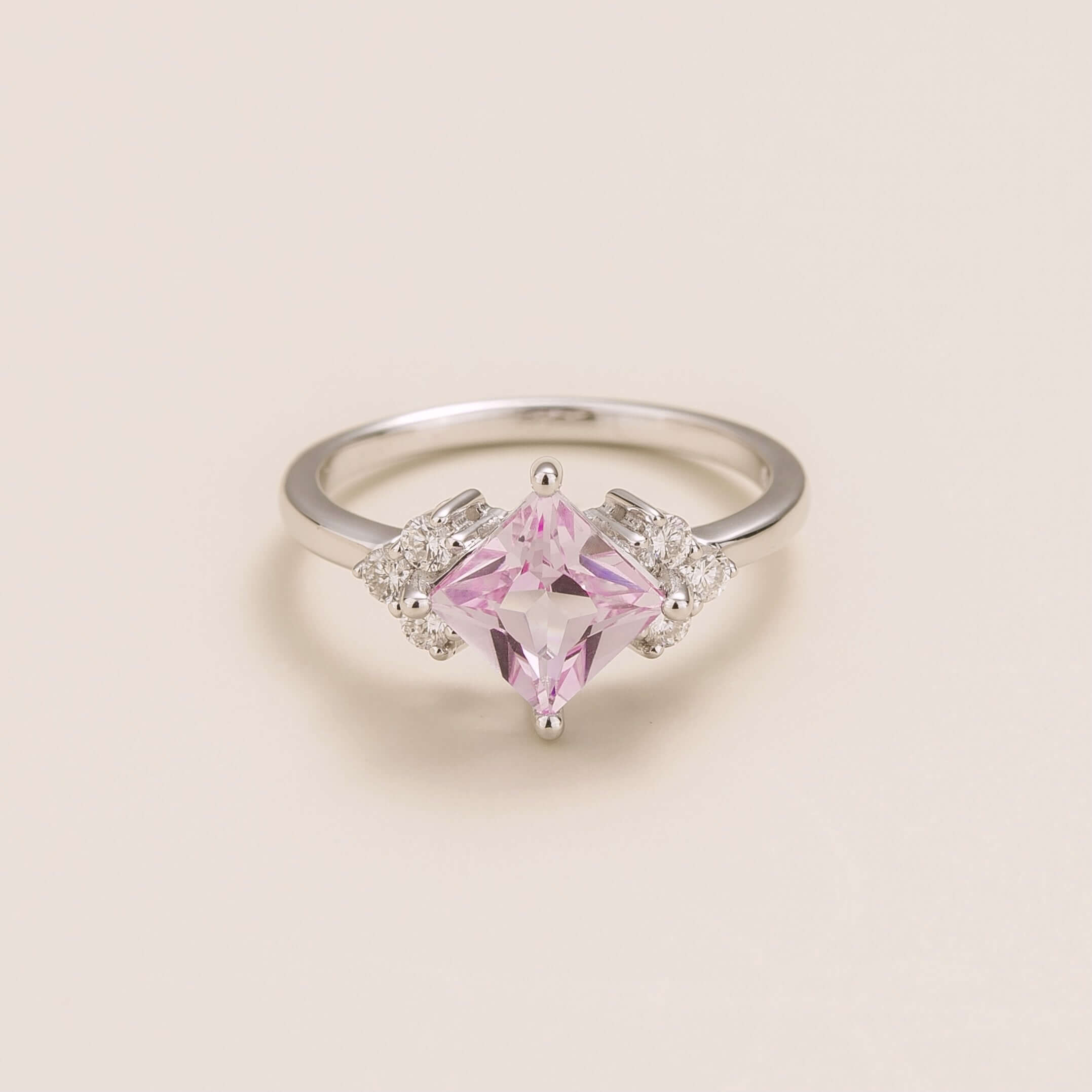 A white gold ring with a princess-cut pink sapphire center stone and smaller diamond accents on the band.