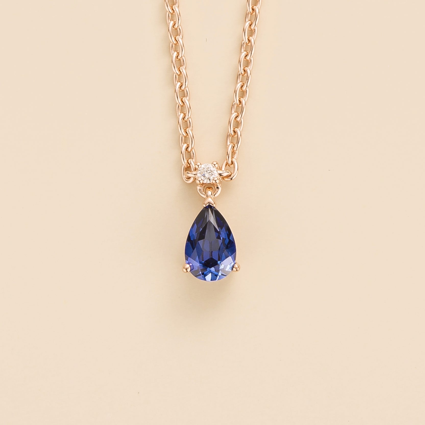 A rose gold necklace with a blue sapphire pendant and a diamond set in a gold-tone band.