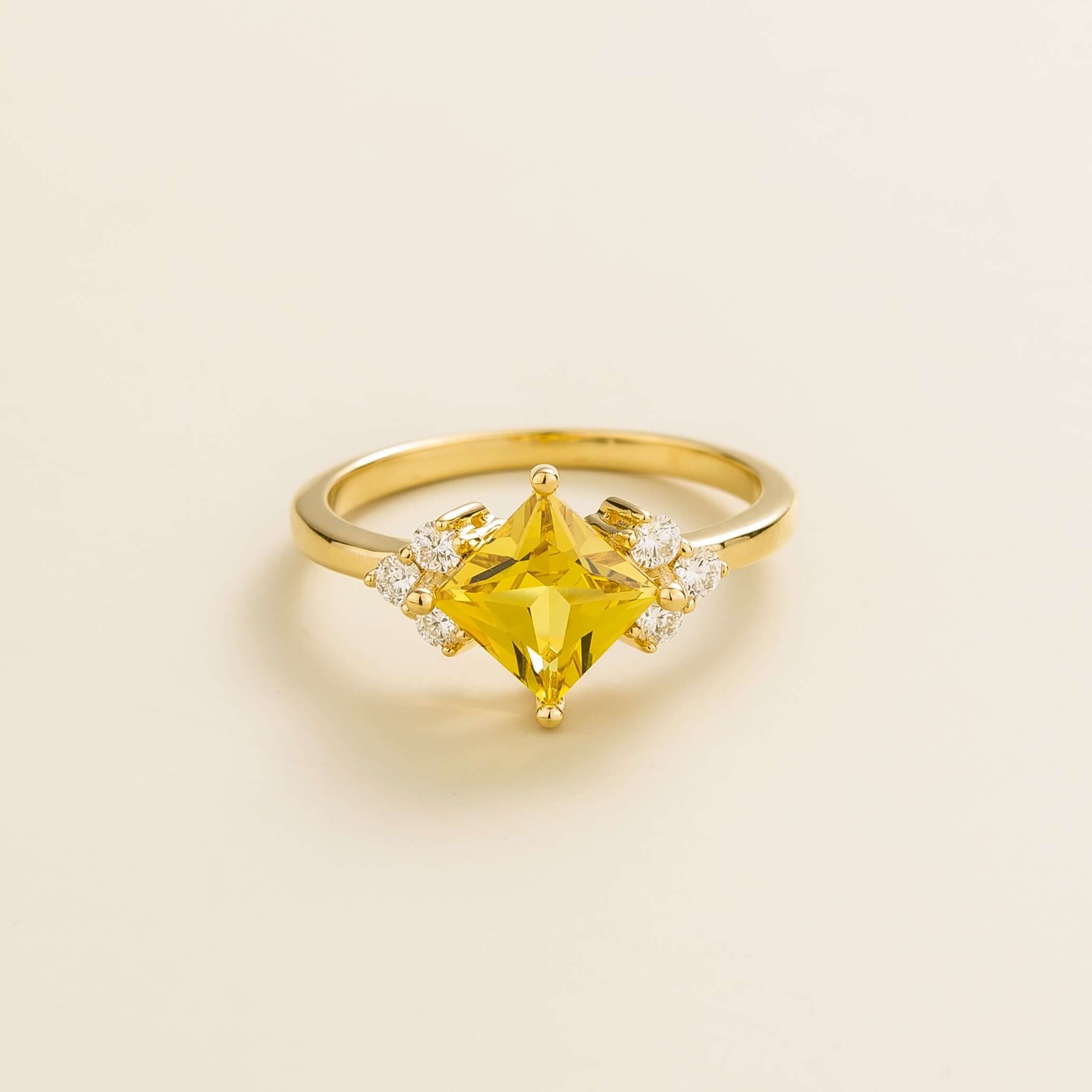 A white gold ring with a princess-cut yellow sapphire center stone and smaller diamond accents on the band.