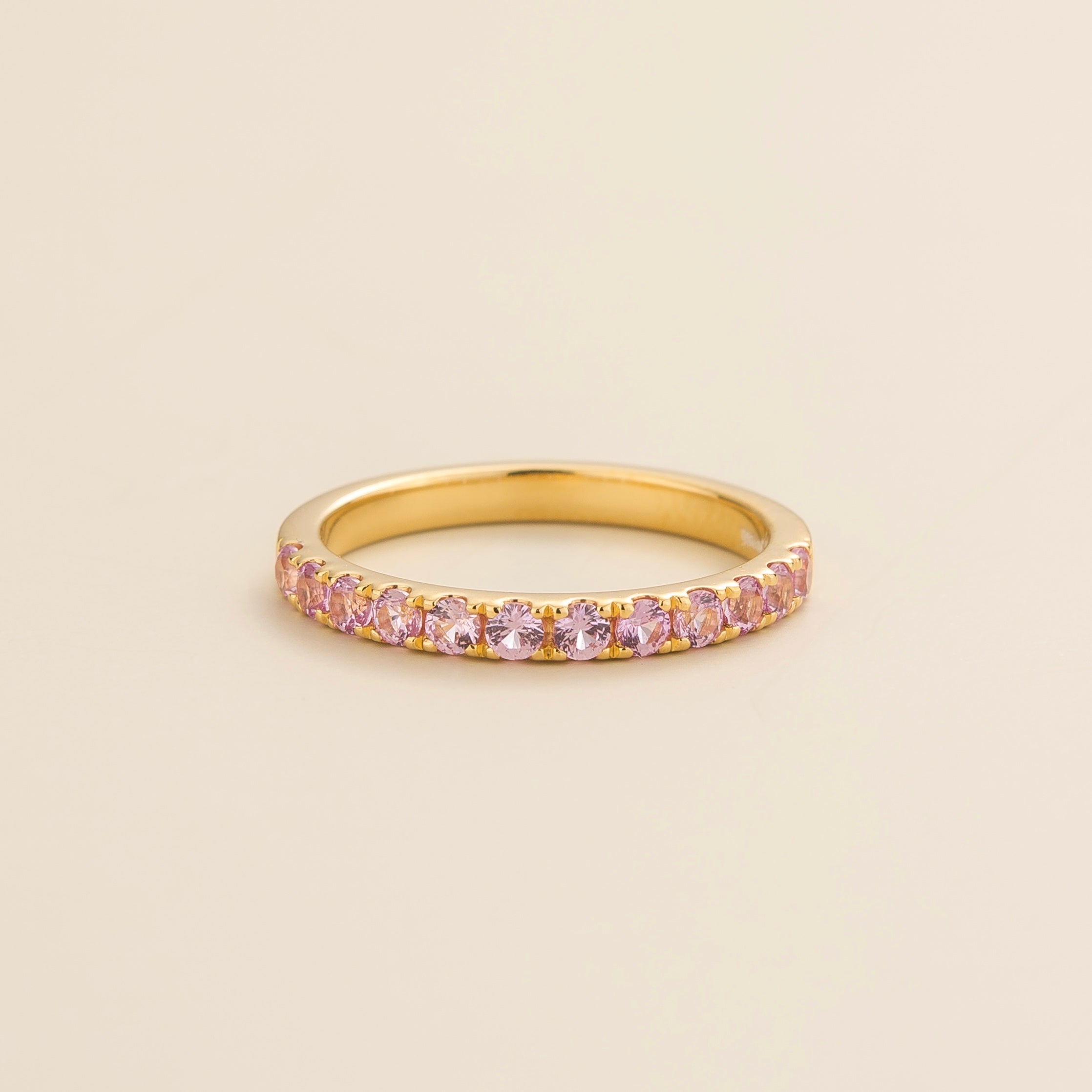 Half eternity gold ring set with pink sapphire gemstones, displayed against a beige background.