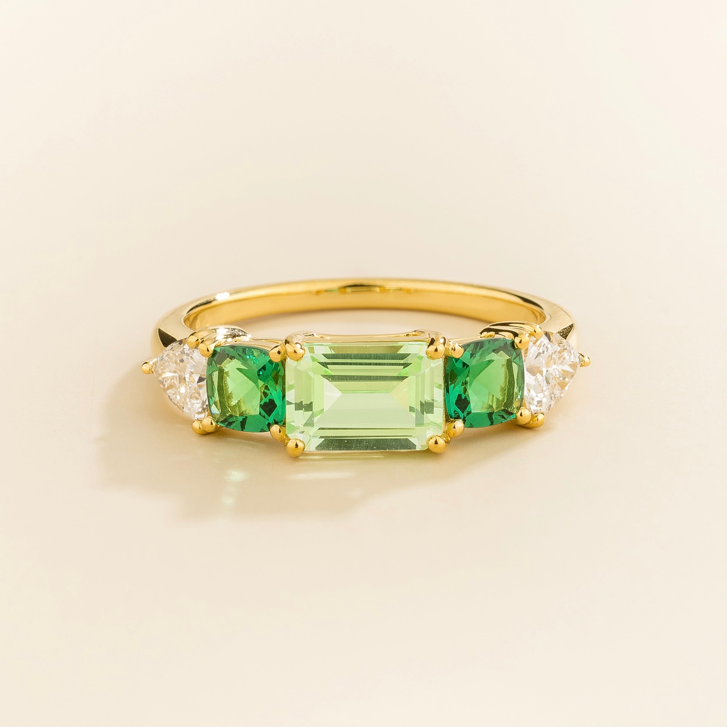 Juvetti yellow gold ring featuring an emerald-cut green sapphire with cushion cut emerald and trillion diamond side stones.