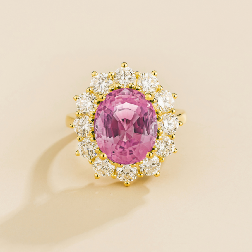 Juvetti yellow gold halo ring featuring an oval lab-grown pink sapphire surrounded by round lab-grown diamonds.
