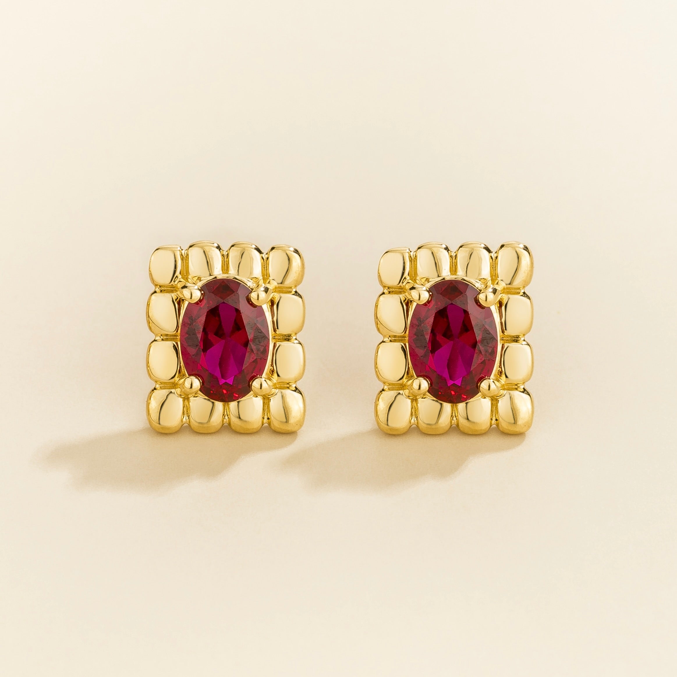 Gold earrings with red ruby gemstones and gold block surrounding details.