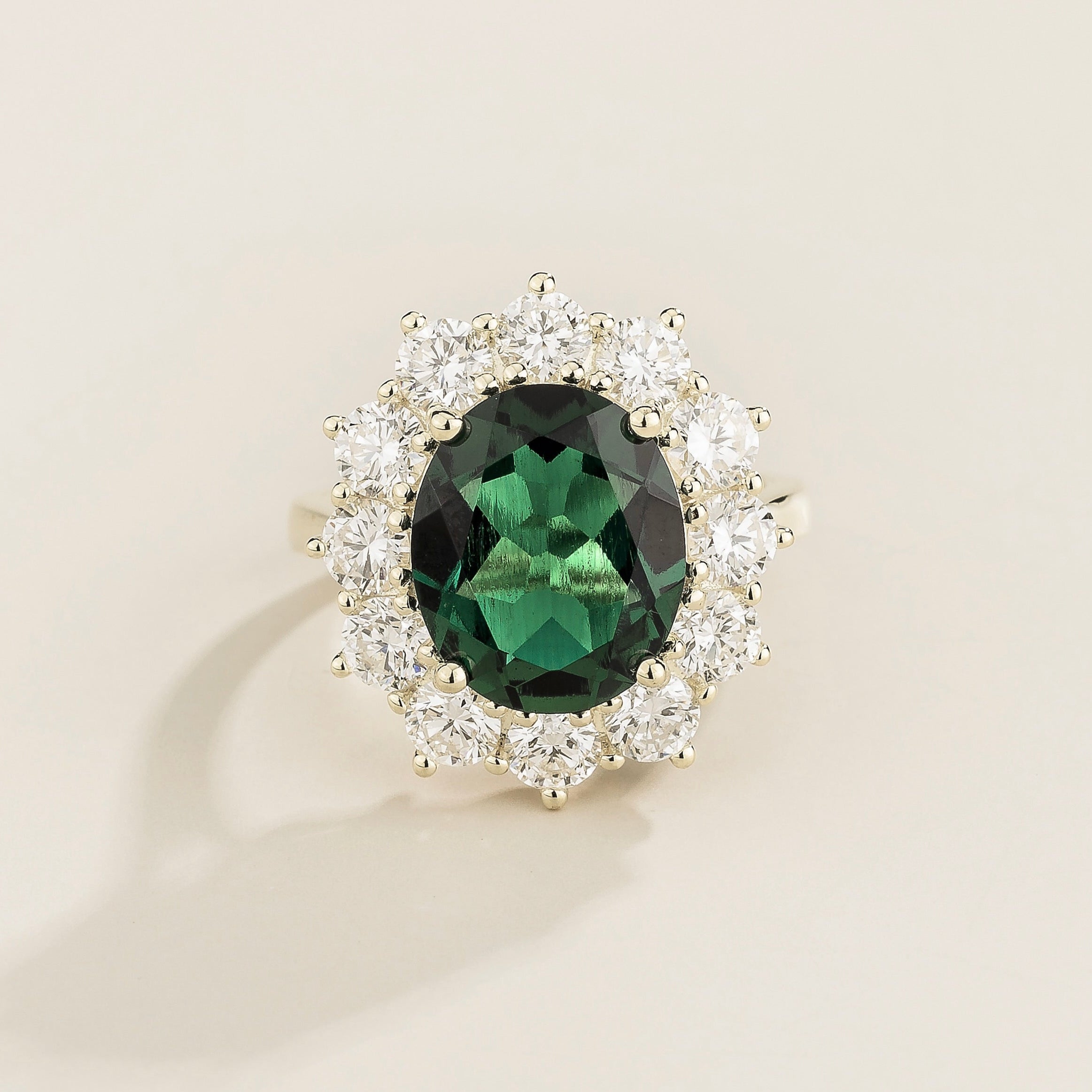 White gold ring with a central emerald and halo of smaller diamonds around it, displayed against a neutral background.