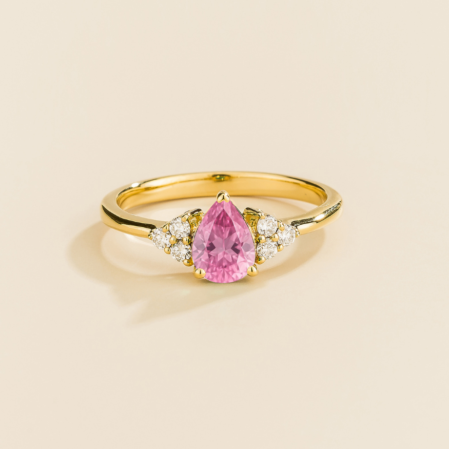 Juvetti yellow gold ring featuring a pear-cut lab-grown pink sapphire with lab-grown diamond side stones.