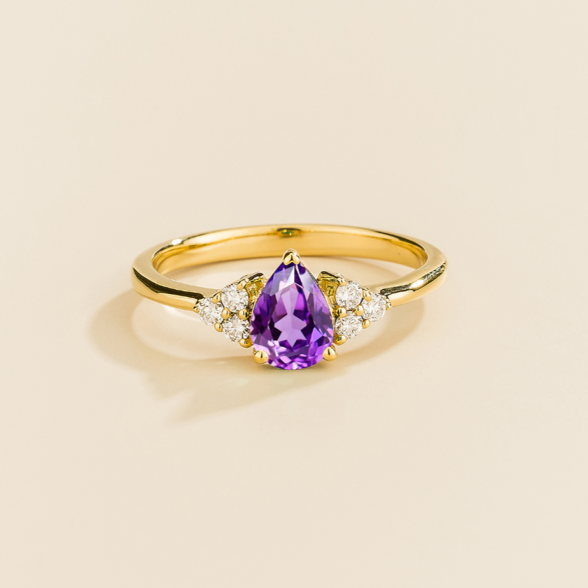 Juvetti yellow gold ring featuring a pear-cut lab-grown purple sapphire with lab-grown diamond side stones.