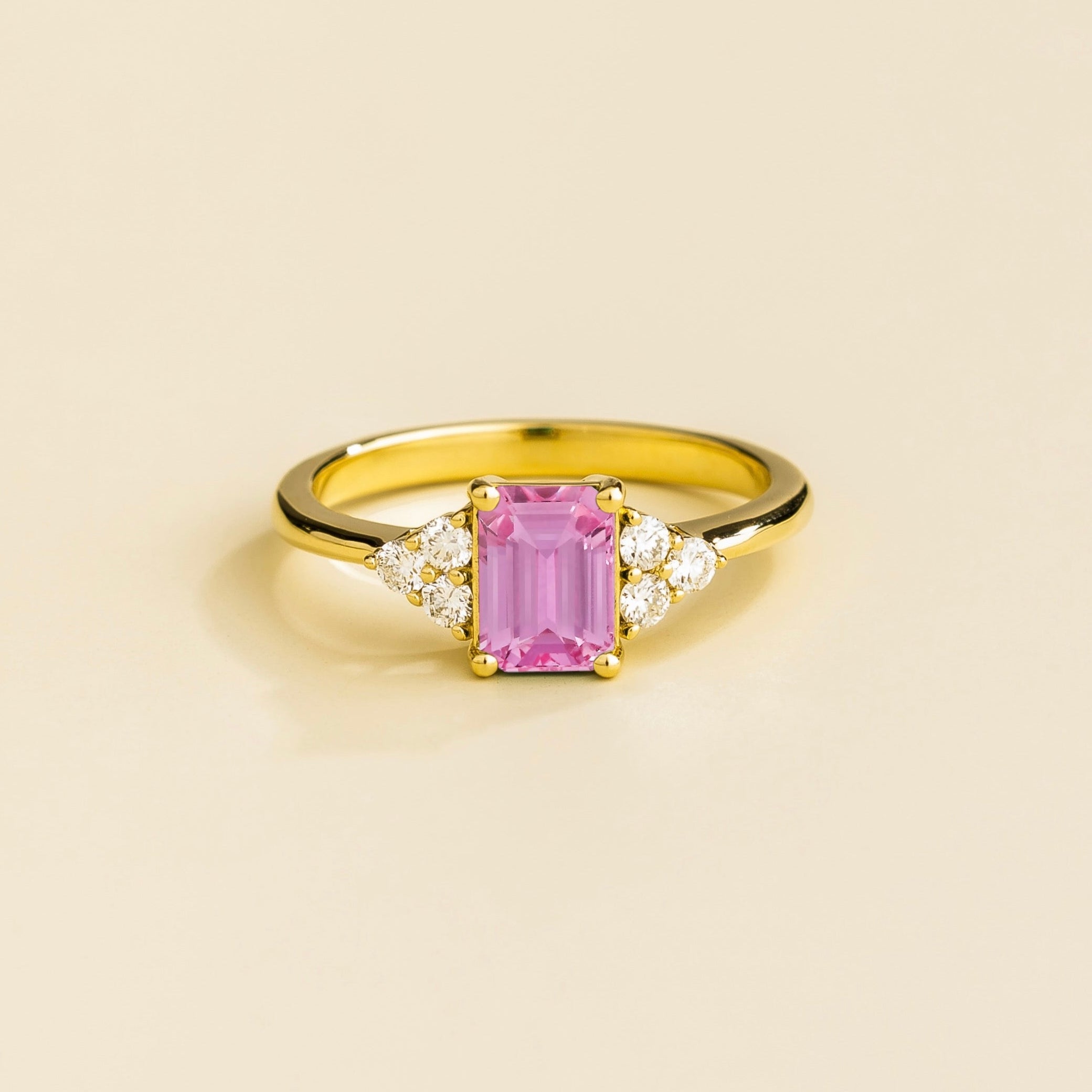 A gold ring featuring a pink sapphire gemstone and small diamonds, set in a classic six-prong setting on a plain band.