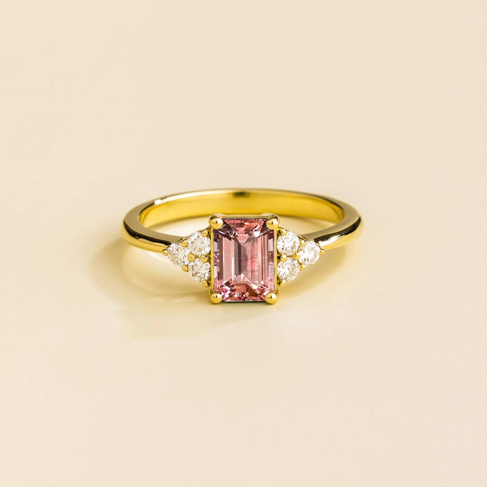 A gold ring with an emerald-cut morganite centerpiece and smaller diamonds around it, displayed against a light background.