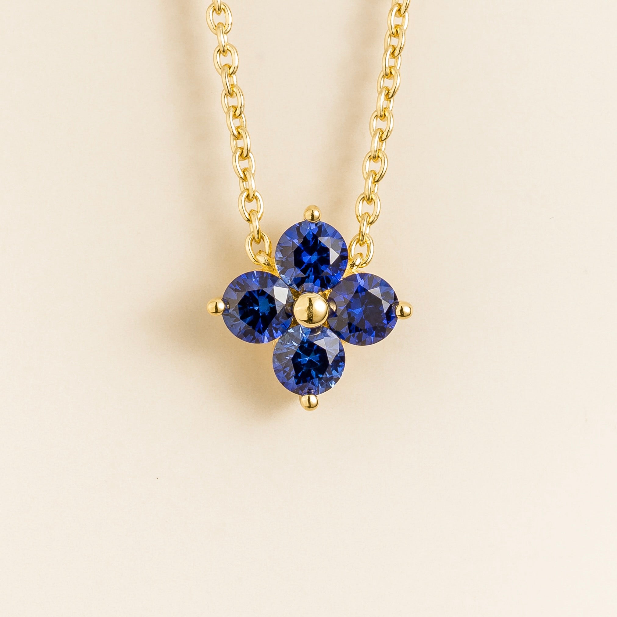 Juvetti yellow gold necklace featuring a clover pendant set with round lab-grown blue sapphires.