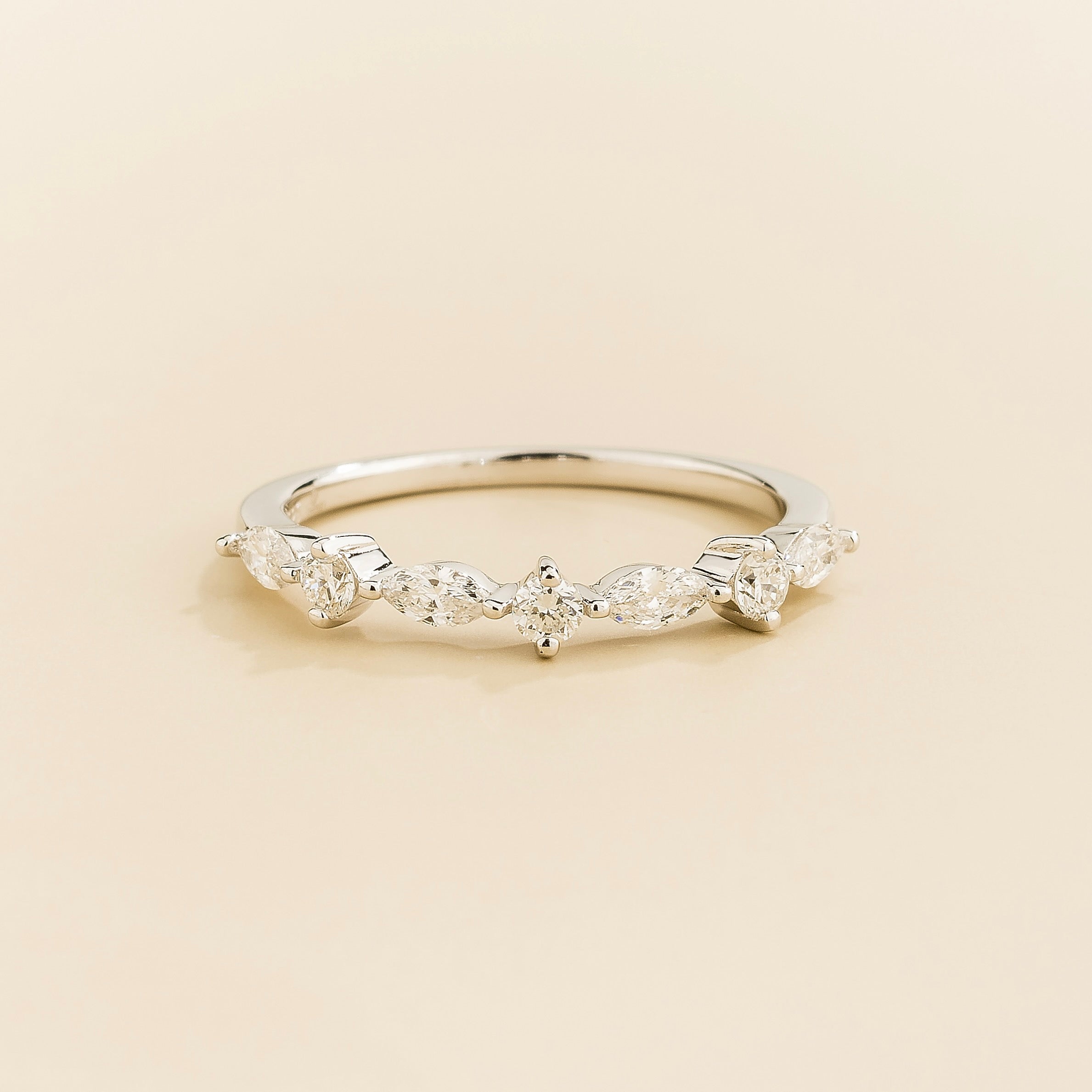A white gold band ring with marquise and round cut diamonds set in an alternating pattern on a plain 