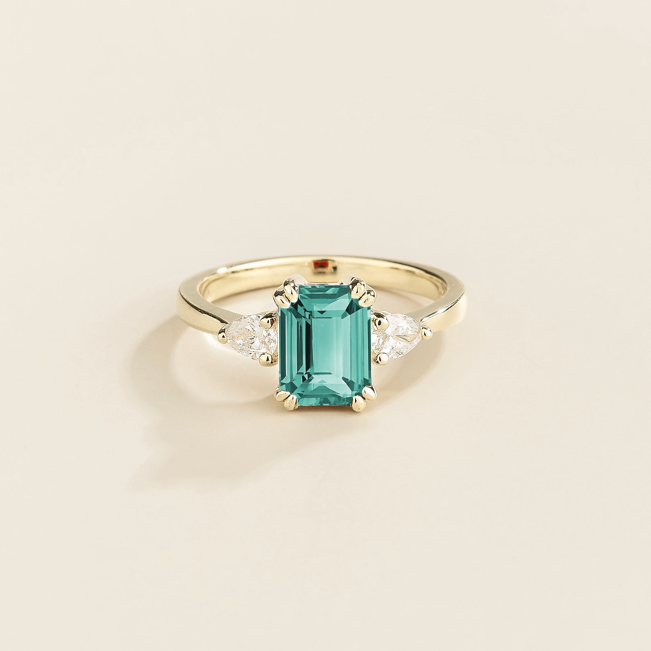 A ring with a paraiba sapphire center stone and pear shape diamonds set in white gold, emerald/octagon cut for the sapphire.