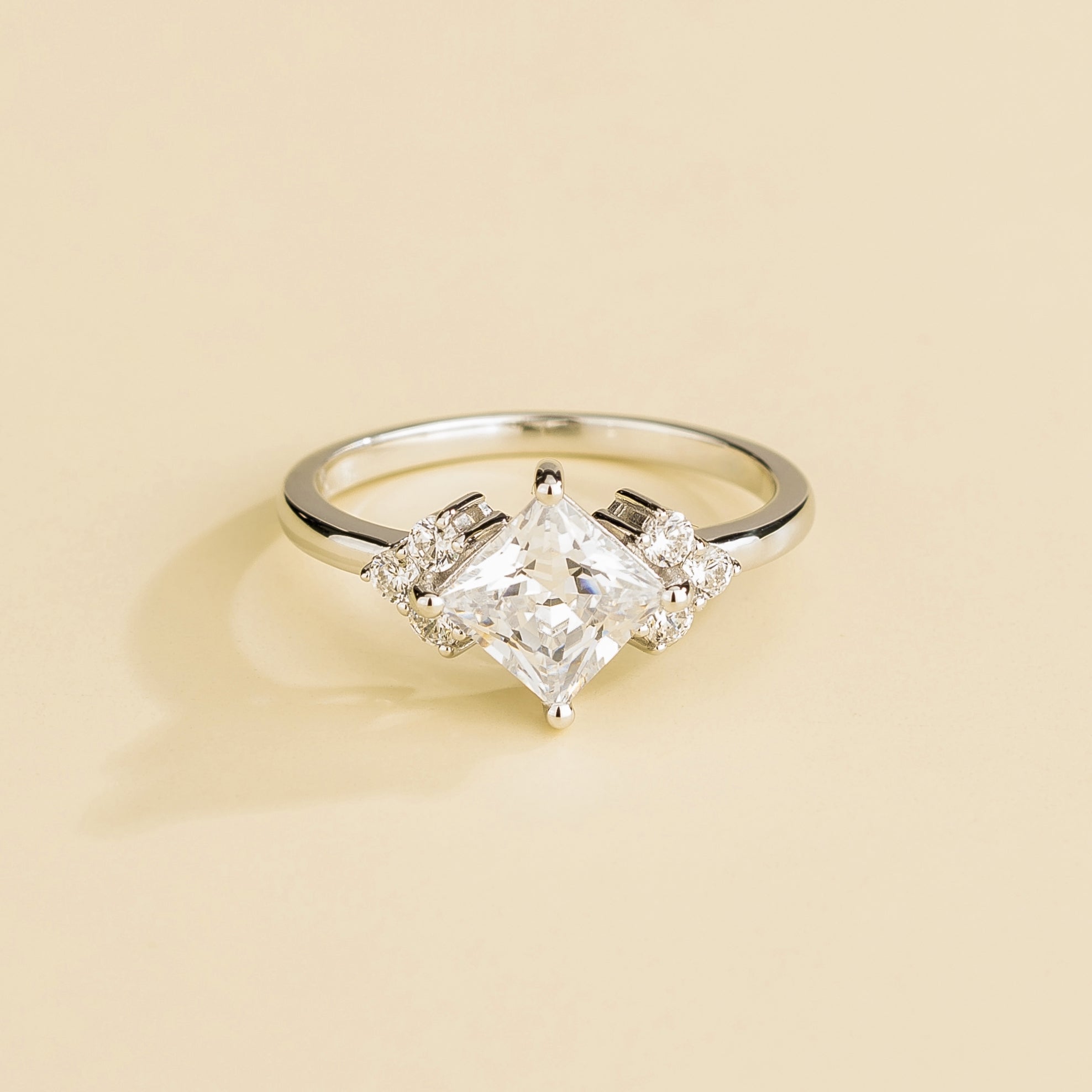 A white gold ring with a central princess cut diamond and accent side diamonds set in a classic six-princess-cut style.